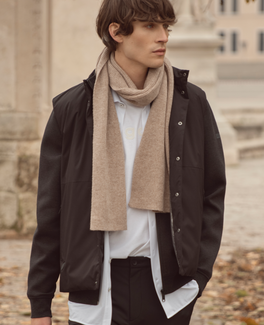 Ein Mann trägt eine schwarze Jacke über Hemd und Pullover, kombiniert mit einem beigefarbenen Schal. Der Look wirkt elegant, modern und perfekt für kühle Tage.