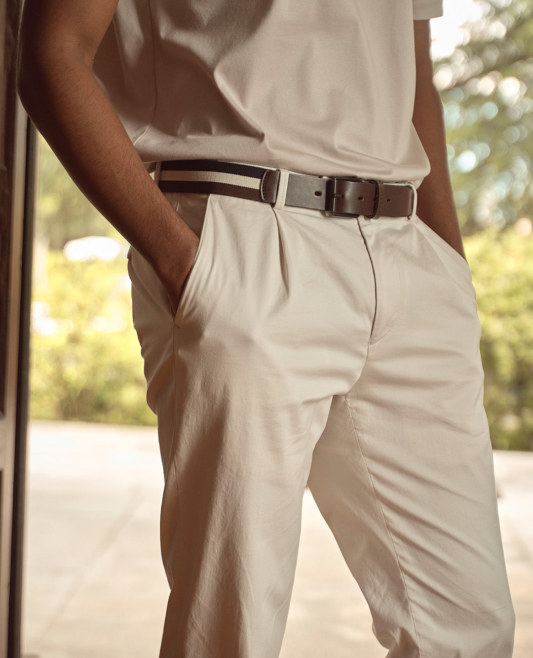 Nahaufnahme eines Mannes in heller Stoffhose mit schwarzem Gürtel und Händen in den Taschen. Lässiger, eleganter Look mit sommerlicher Leichtigkeit.