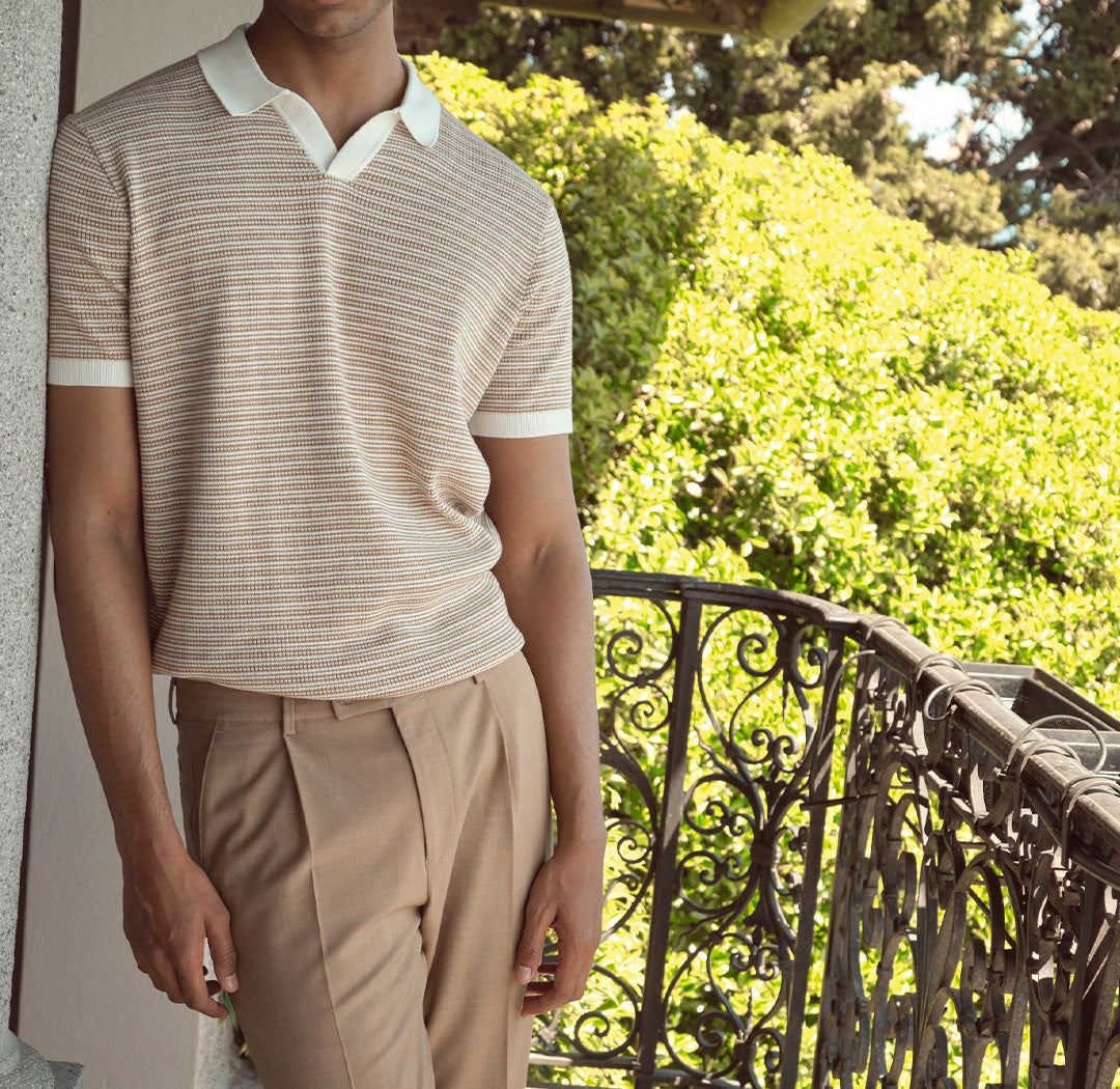 Ein Mann trägt ein kurzärmliges Strickpolo mit feinem Streifenmuster und eine beige Stoffhose. Der Look wirkt sommerlich, elegant und gepflegt leger.