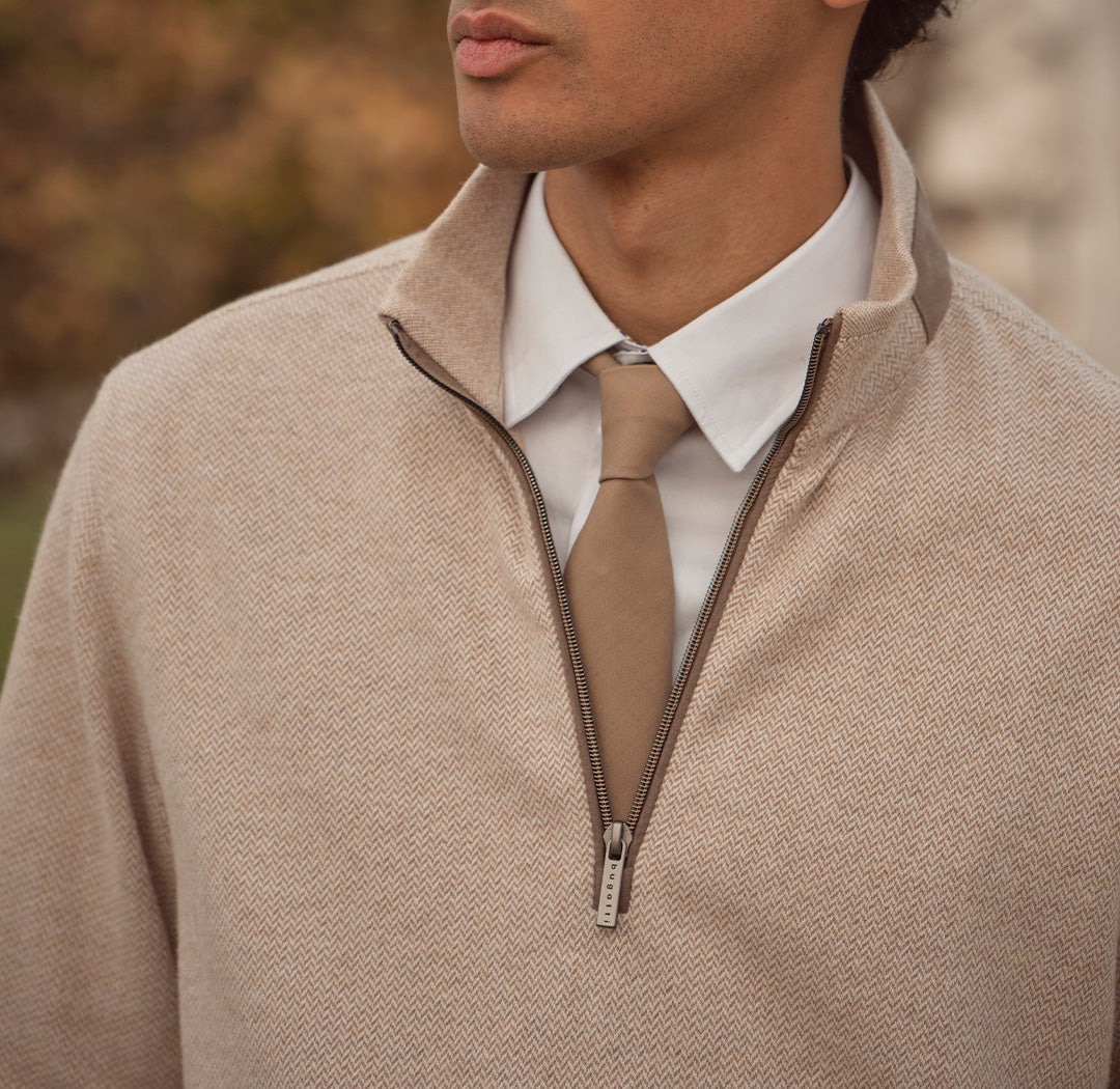 Nahaufnahme eines Mannes in beigem Half-Zip-Pullover über weißem Hemd mit beigefarbener Krawatte. Stilvoller, eleganter Look mit modernem Twist.