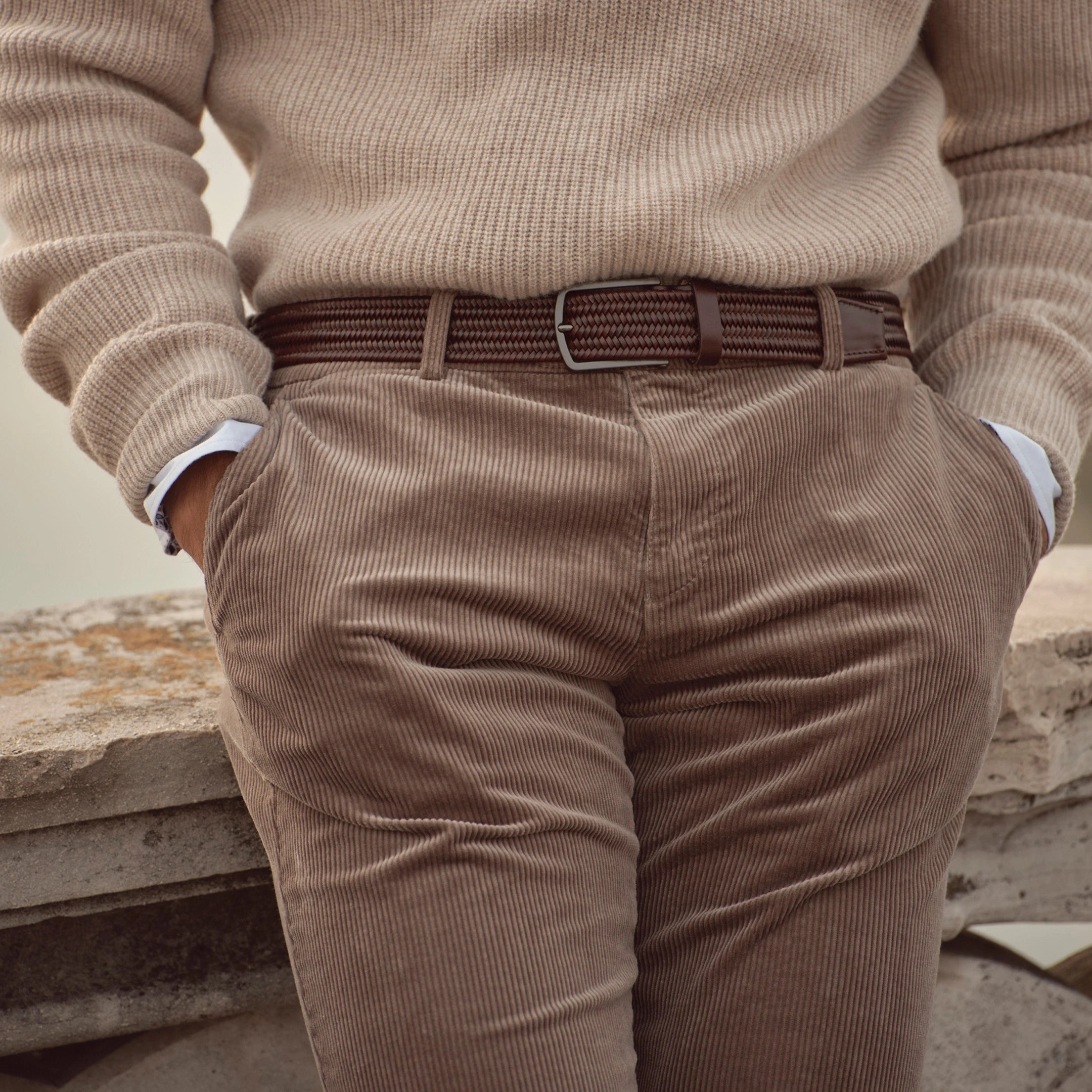 Nahaufnahme eines Herrenlooks aus der bugatti Herbst/Winter-Kollektion 2025: beigefarbener Strickpullover kombiniert mit brauner Cordhose und passendem Gürtel – moderner Casual Chic im Venetian Style.