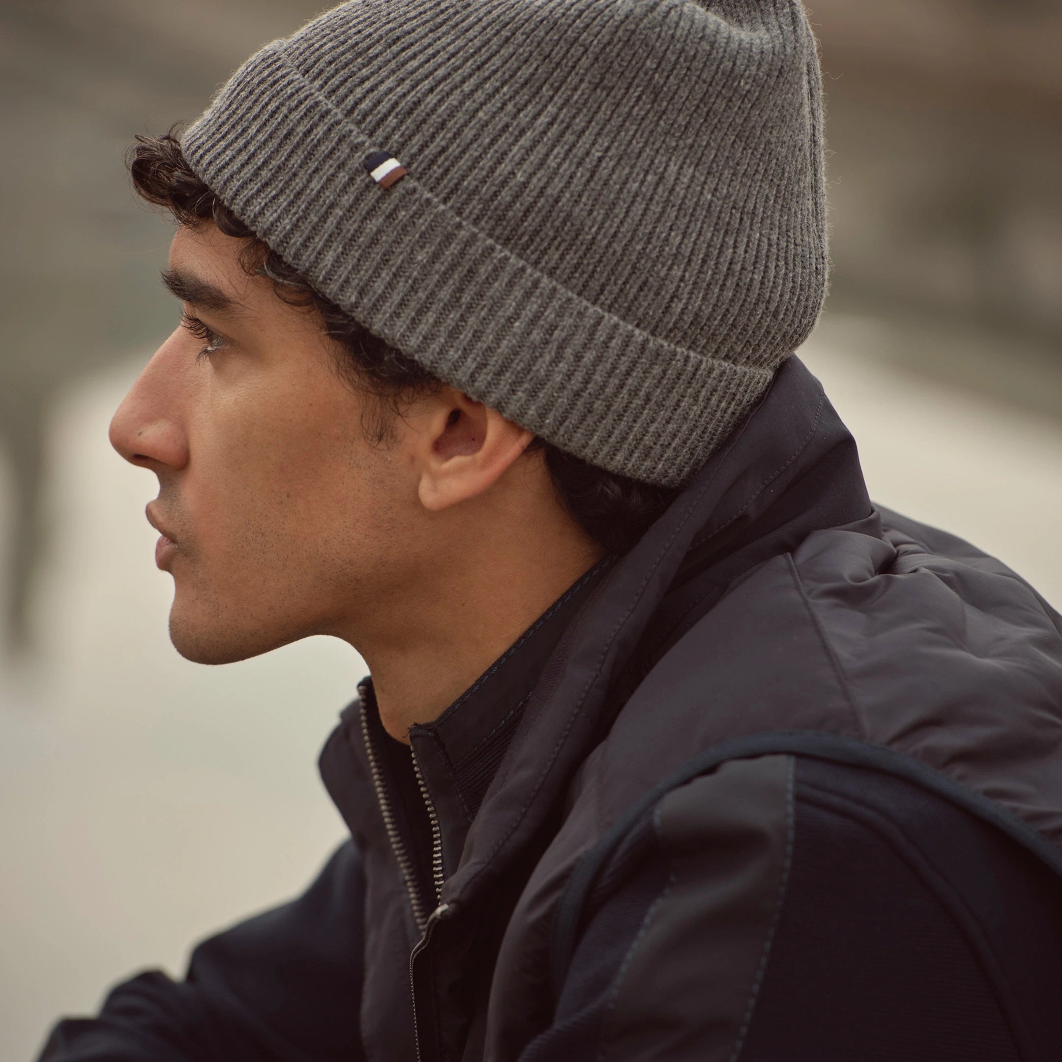 Mann trägt graue bugatti Strickmütze kombiniert mit dunkelblauer Steppweste – modernes Accessoire und Casual Look der Herren Herbst/Winter-Kollektion 2025 im Venetian Chic.