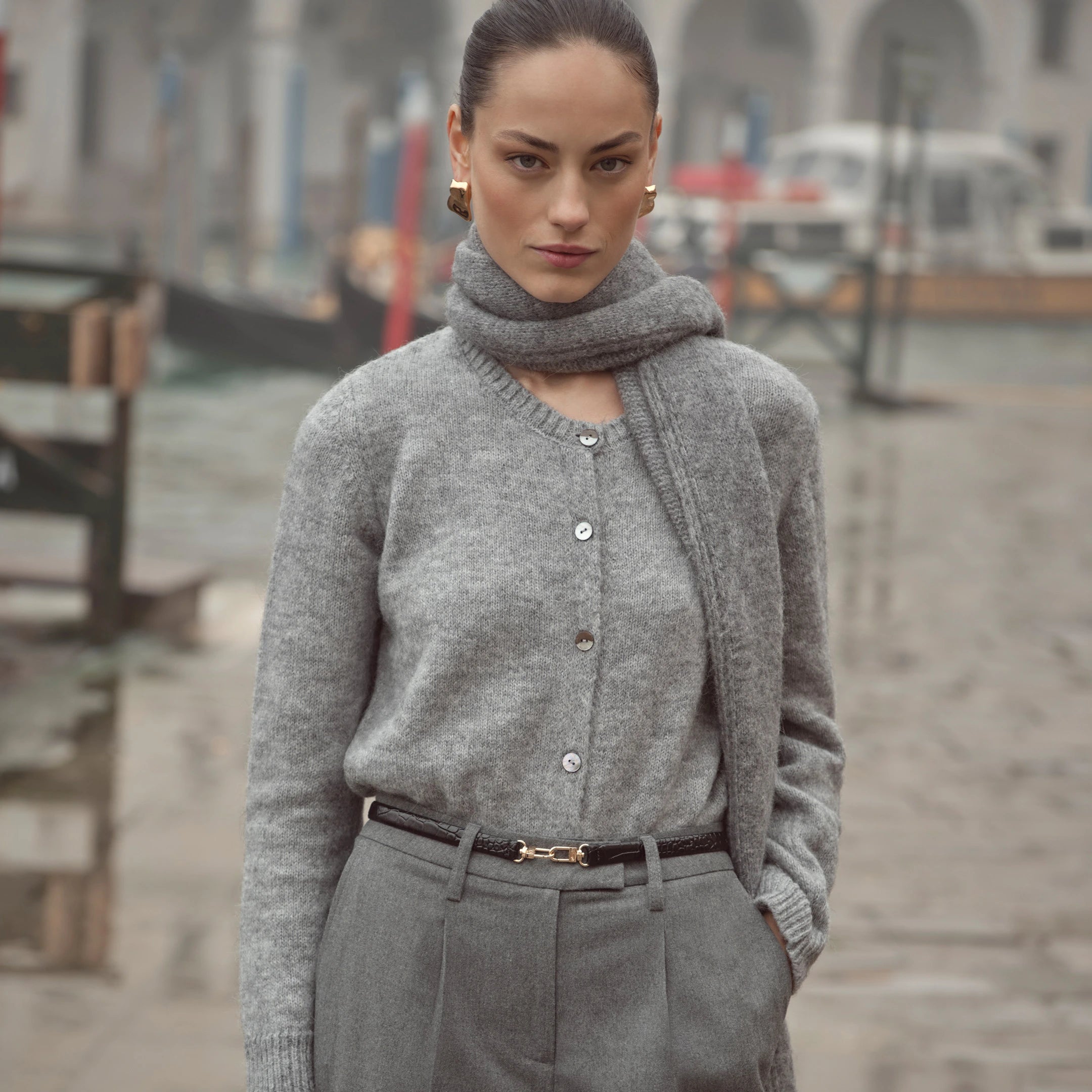 Frau trägt grauen bugatti Cardigan mit Knopfleiste und passendem Schal, kombiniert mit grauer Bundfaltenhose – eleganter Look der Damen Herbst/Winter-Kollektion 2025 im Venetian Chic.