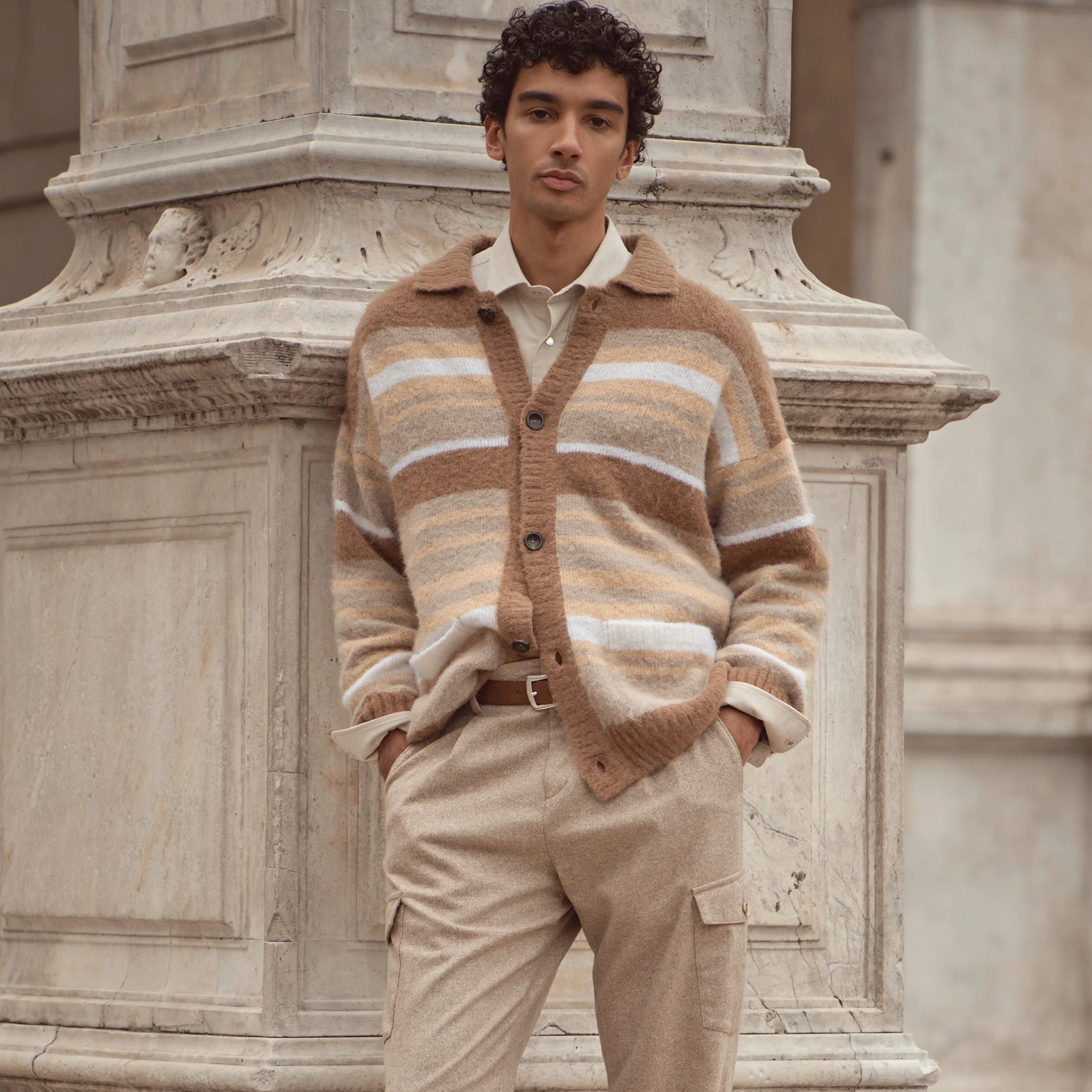 Mann trägt beigefarbene bugatti Cargo-Hose kombiniert mit gestreifter Strickjacke in Naturtönen aus der Herren Herbst/Winter-Kollektion 2025 – moderner Casual Look im Venetian Chic.
