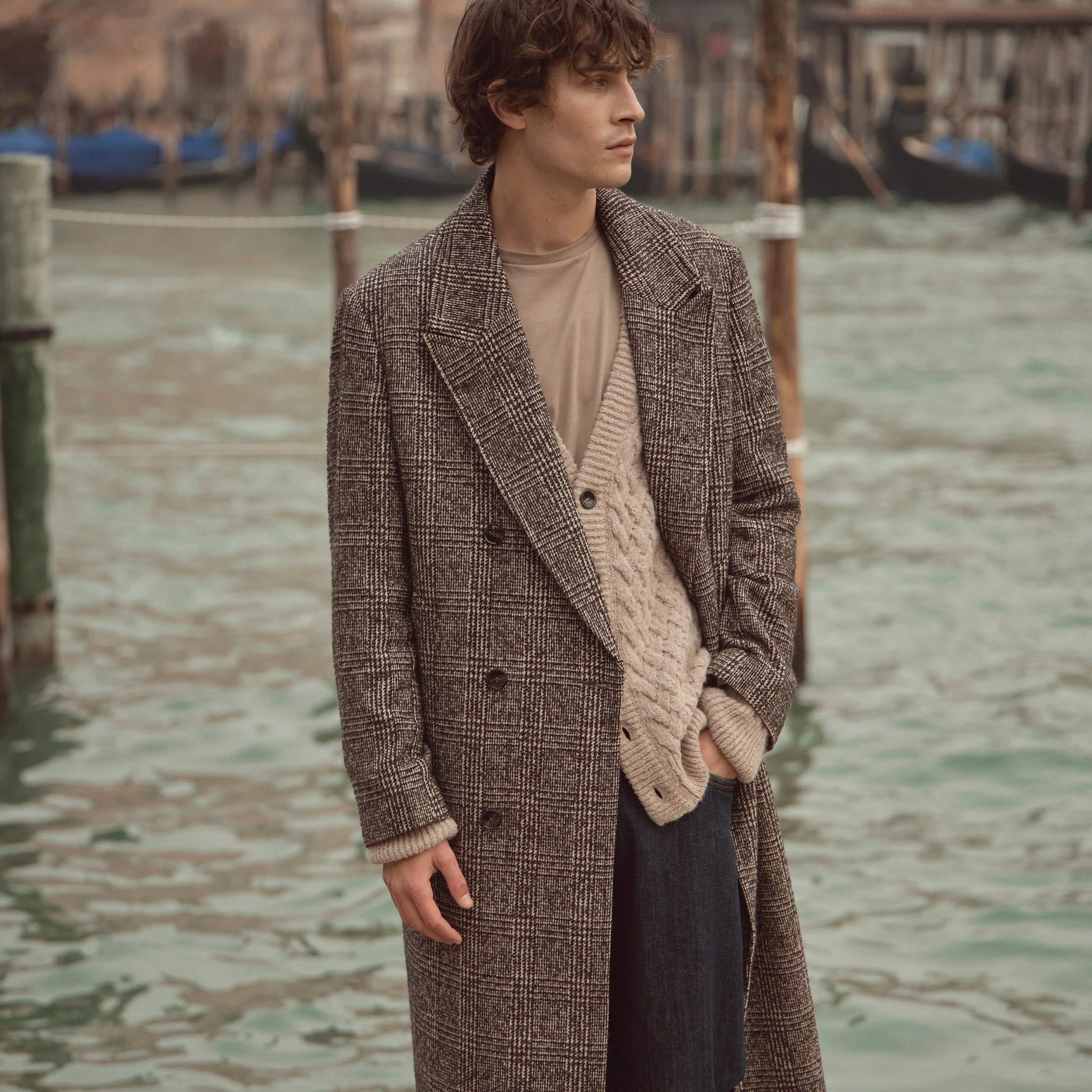 Mann trägt karierten bugatti Wollmantel in Braun-Grau über Strick-Cardigan und T-Shirt aus der Herren Herbst/Winter-Kollektion 2025 – eleganter Look im Venetian Chic, aufgenommen vor den Kanälen Venedigs.