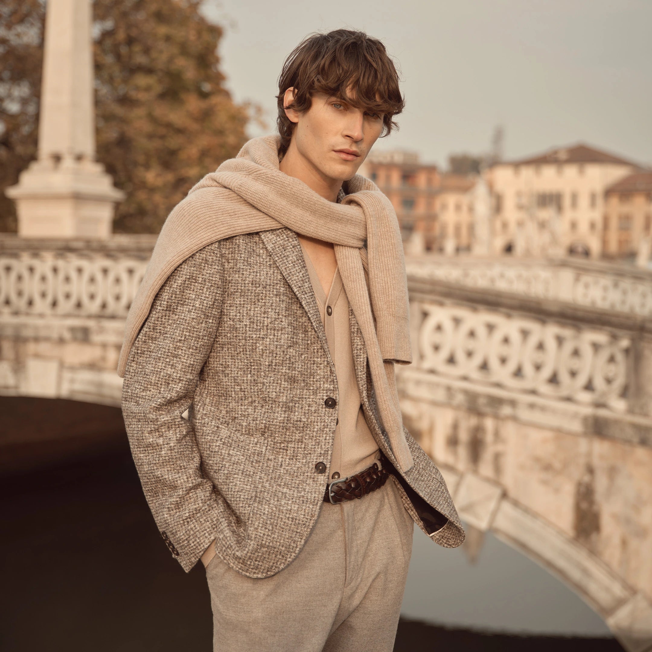 Mann trägt graues bugatti Sakko mit Strukturmuster, kombiniert mit beiger Hose und über die Schultern gelegtem Strickpullover – eleganter Herrenlook der Herbst/Winter-Kollektion 2025 im Venetian Chic.