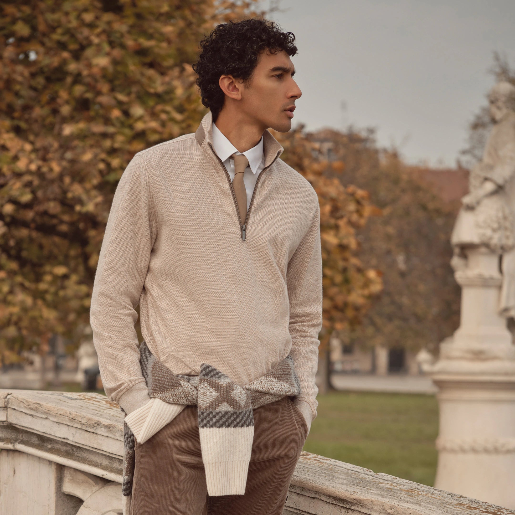 Mann trägt beigefarbenen bugatti Strickpullover mit Zipper über Hemd und Krawatte, kombiniert mit Cordhose – eleganter Herrenlook der Herbst/Winter-Kollektion 2025 im Venetian Chic.