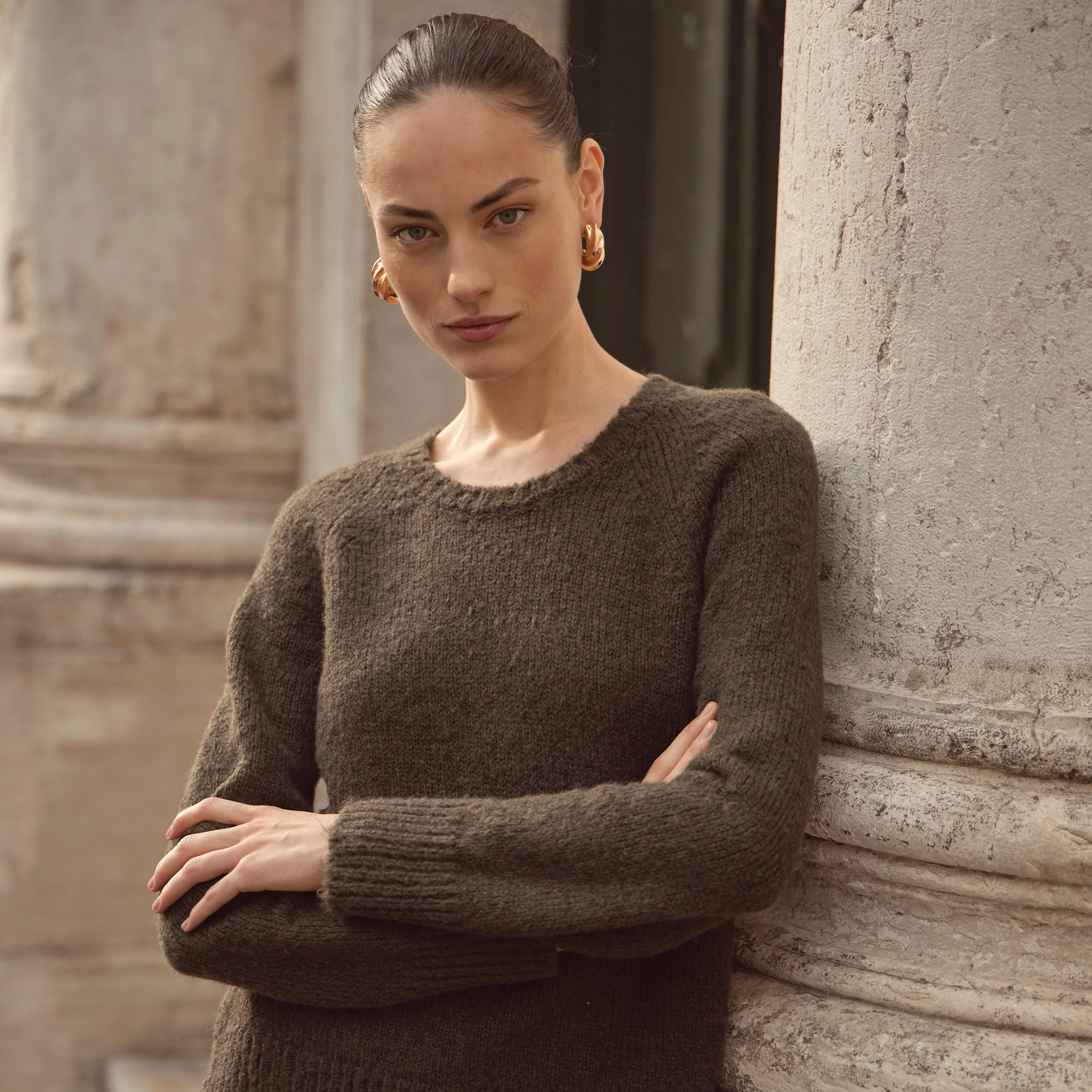 Frau trägt olivgrünen bugatti Strickpullover mit Rundhalsausschnitt aus der Damen Herbst/Winter-Kollektion 2025 – moderner Look im Venetian Chic, elegant kombiniert mit goldenen Creolen.