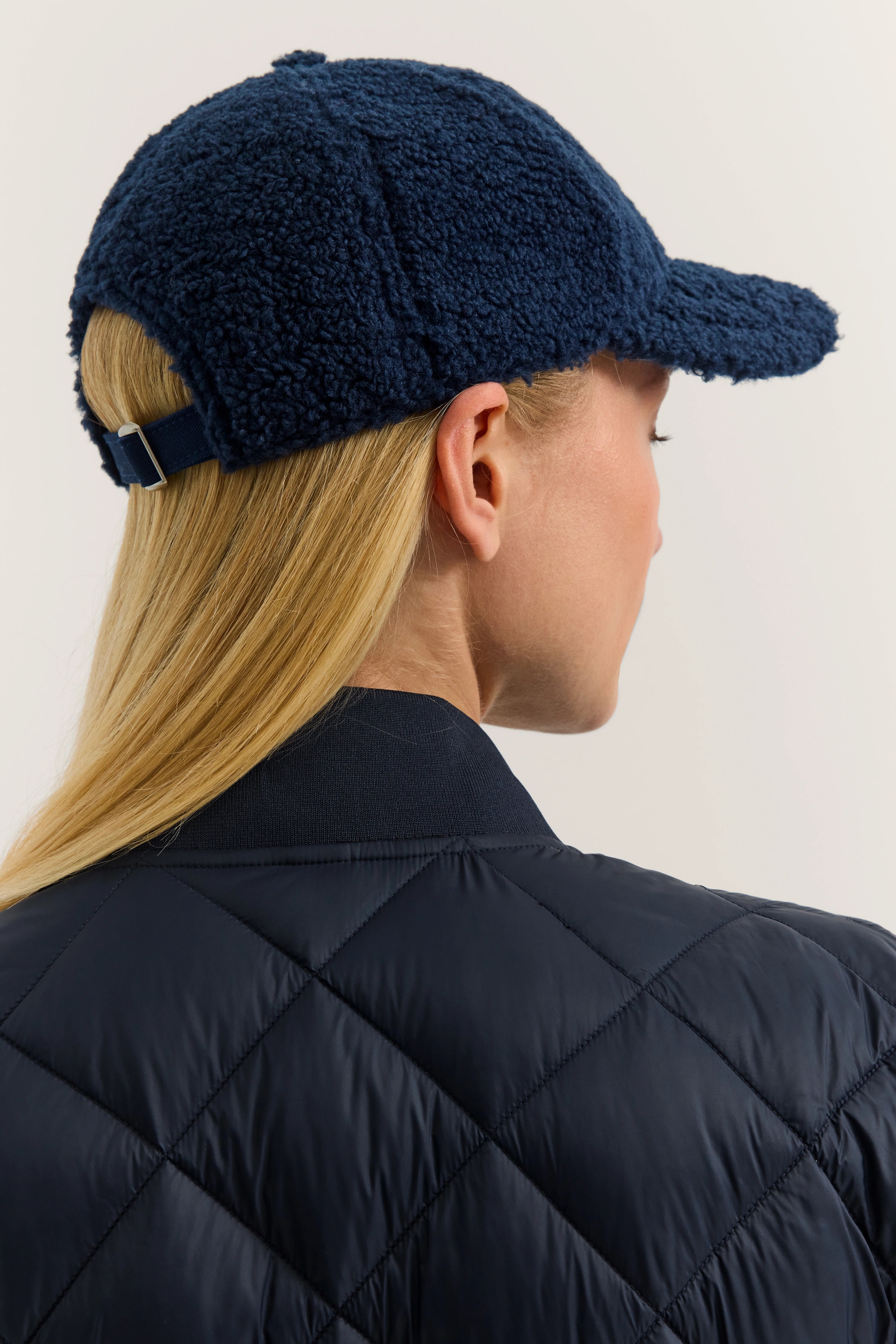 Navy blaue Teddycap und gesteppte Jacke, Model von hinten.