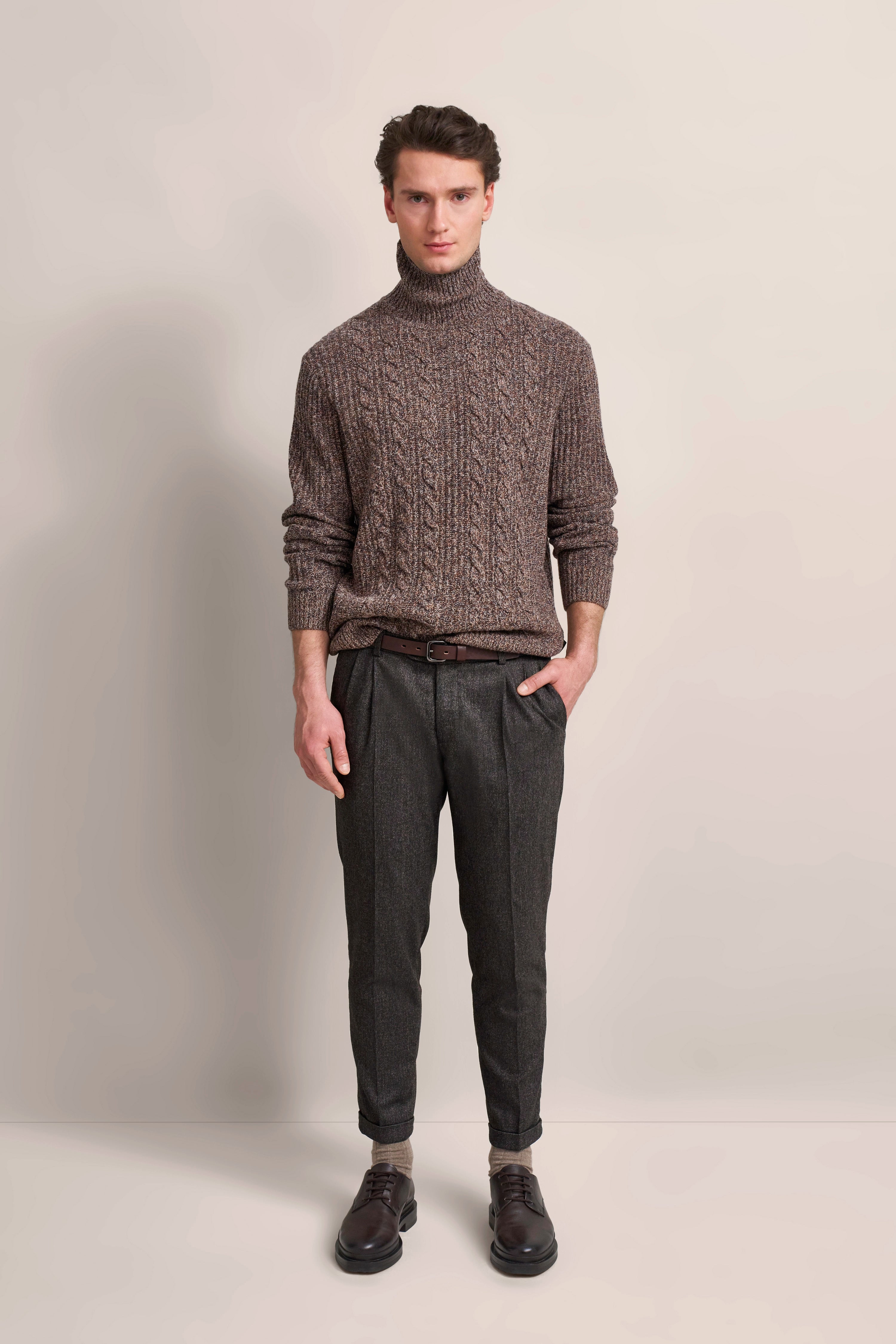 bugatti Modelbild: Brauner Rollkragenpullover und graue Hose, entspanntes Posing.