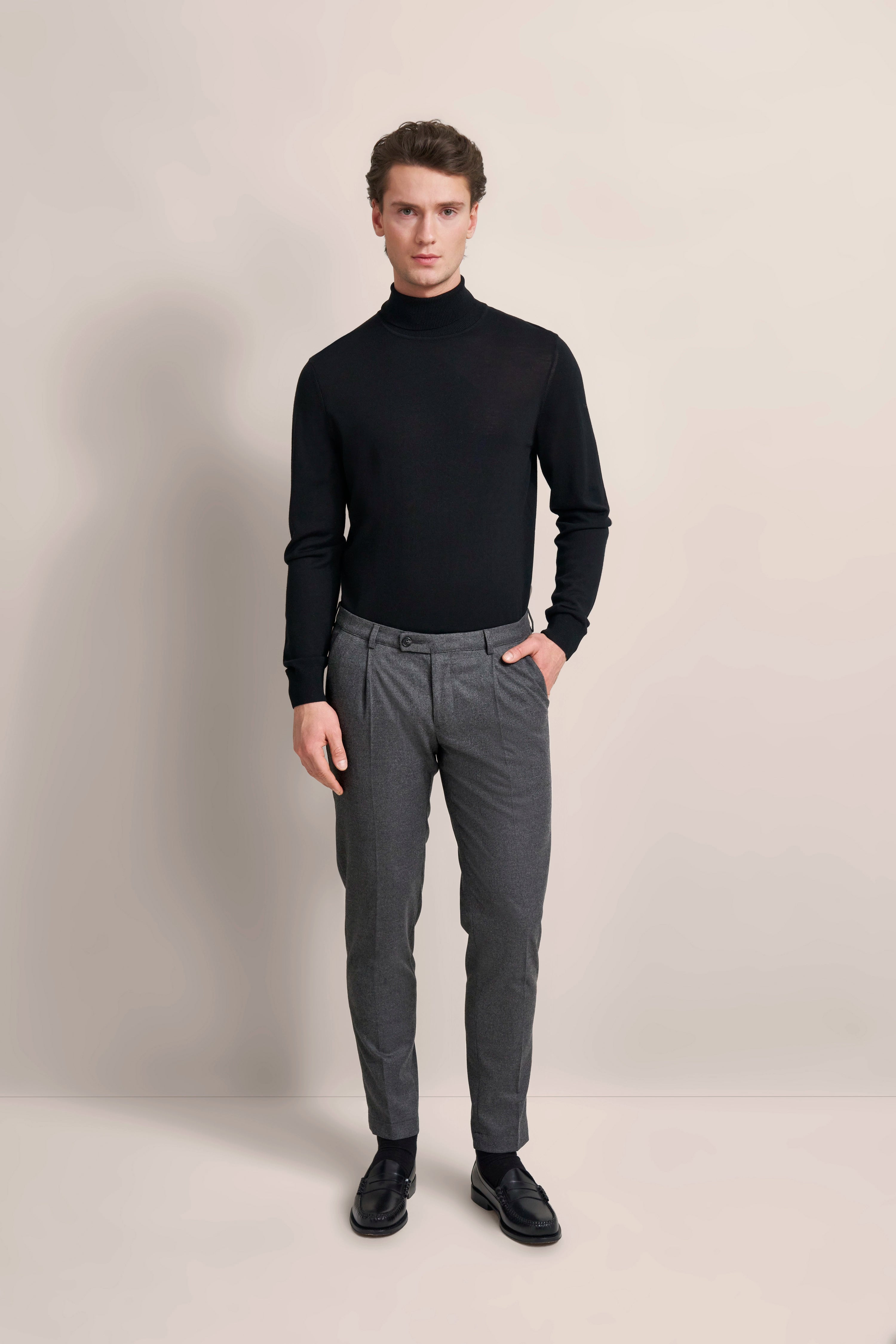 Model in black turtleneck sweater and gray pants, standing frontally, bugatti style.