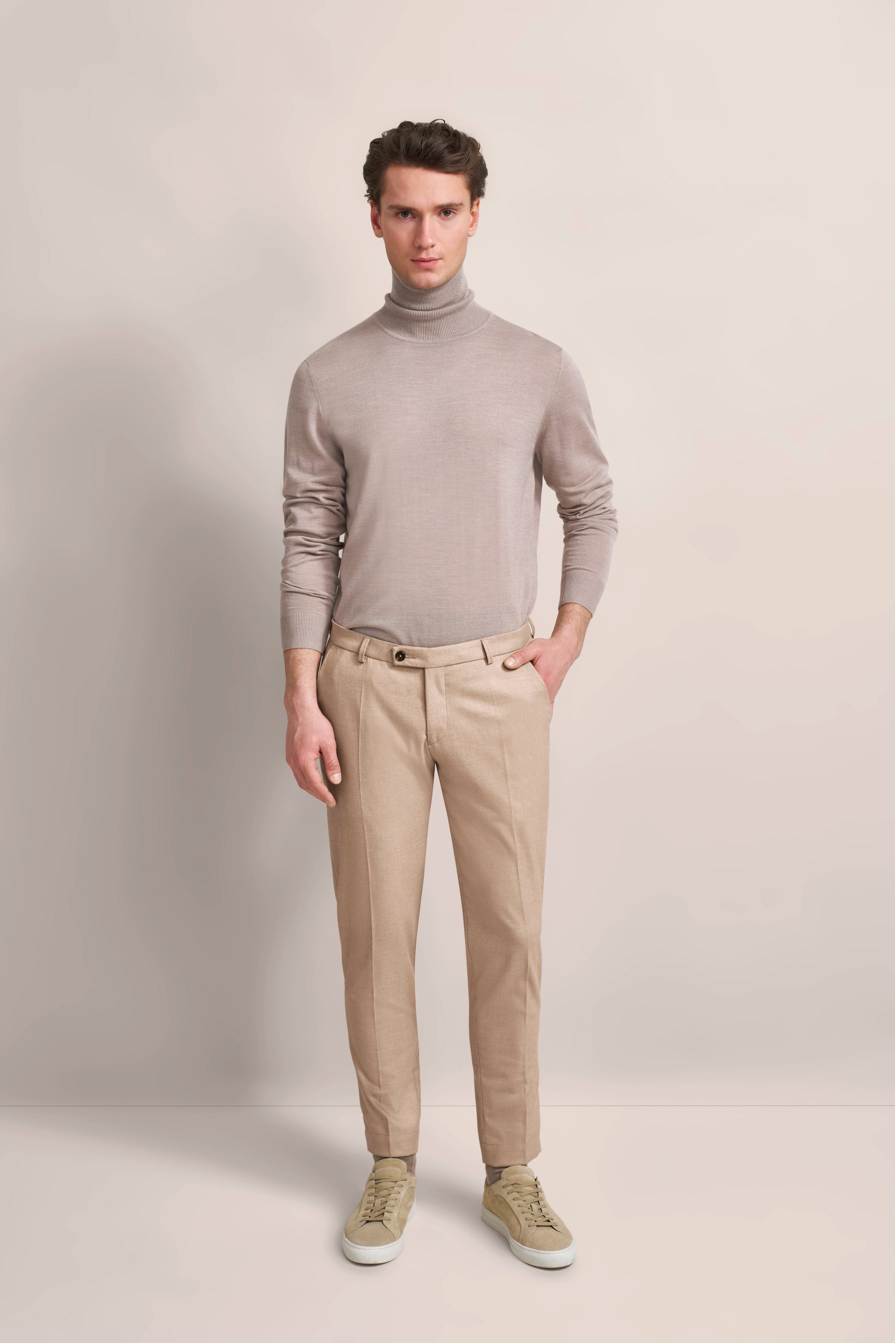 Model in beigem Rollkragenpullover und beigefarbener Hose, stehend, neutraler Hintergrund.