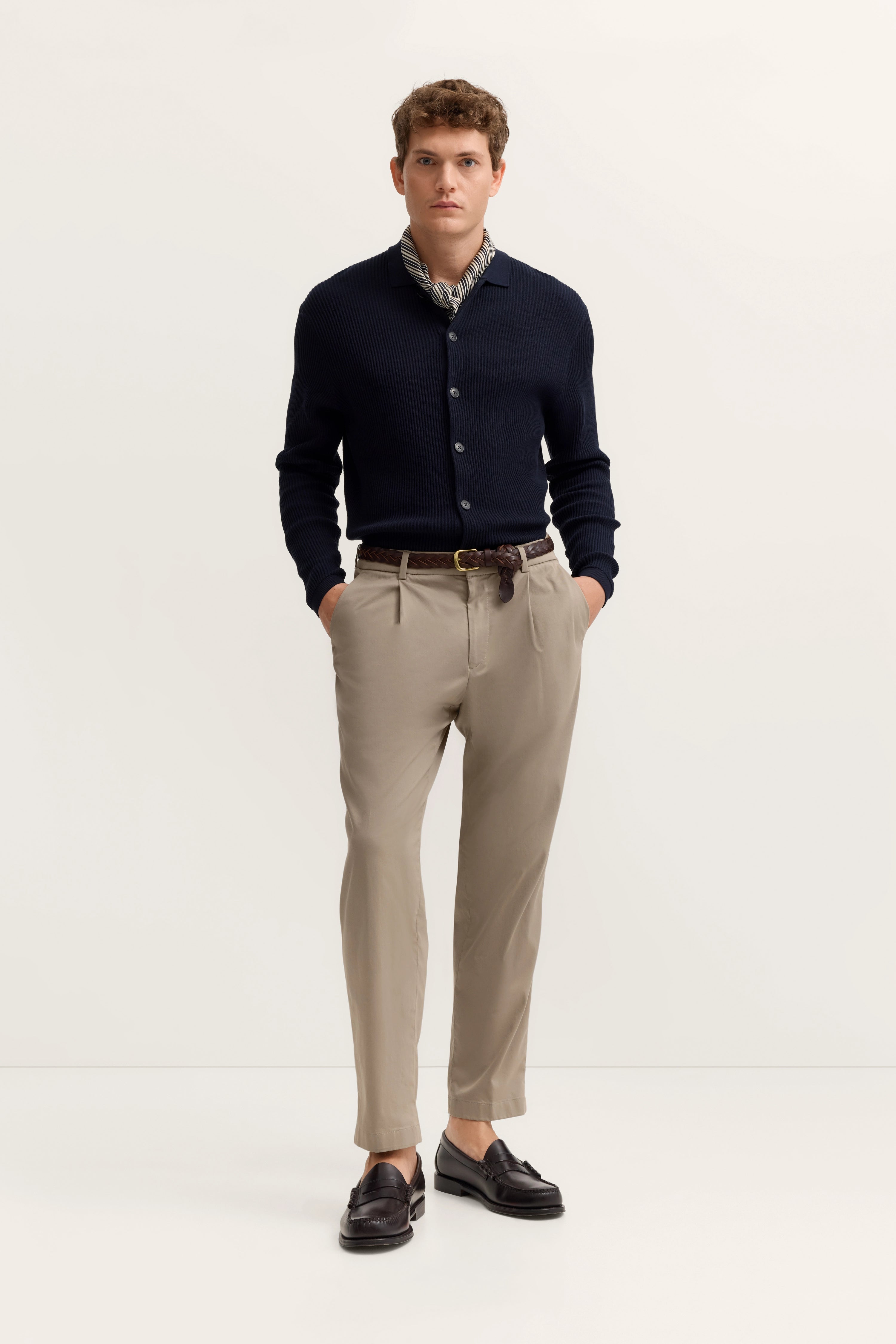 Model trägt navy Strickjacke, gestreiftes Hemd, beige Chinos und braune Loafer von bugatti.