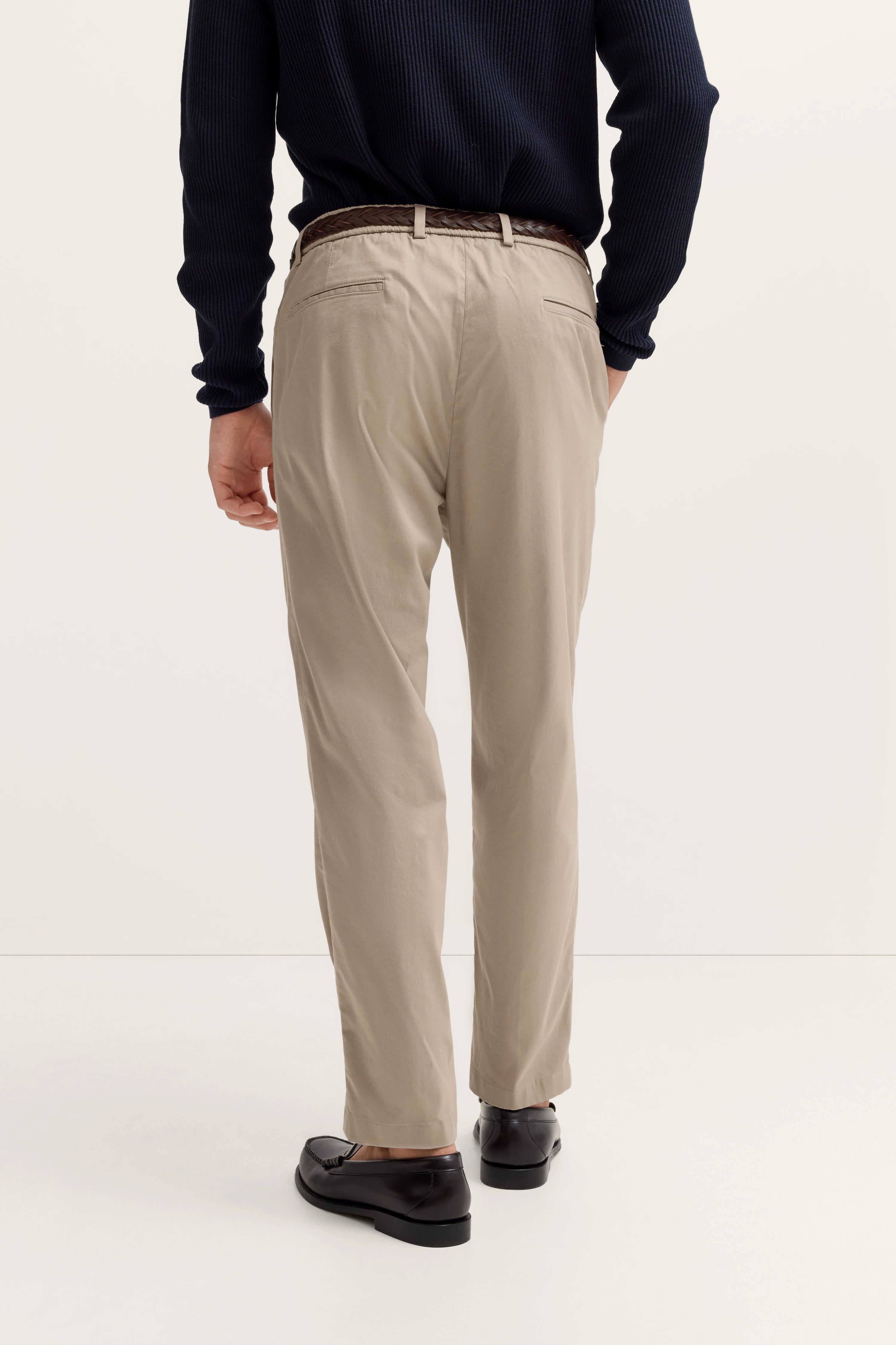 Beige Chino-Hose und schwarzer Pullover, Rückansicht Model, entspanntes Posing, bugatti Stil.