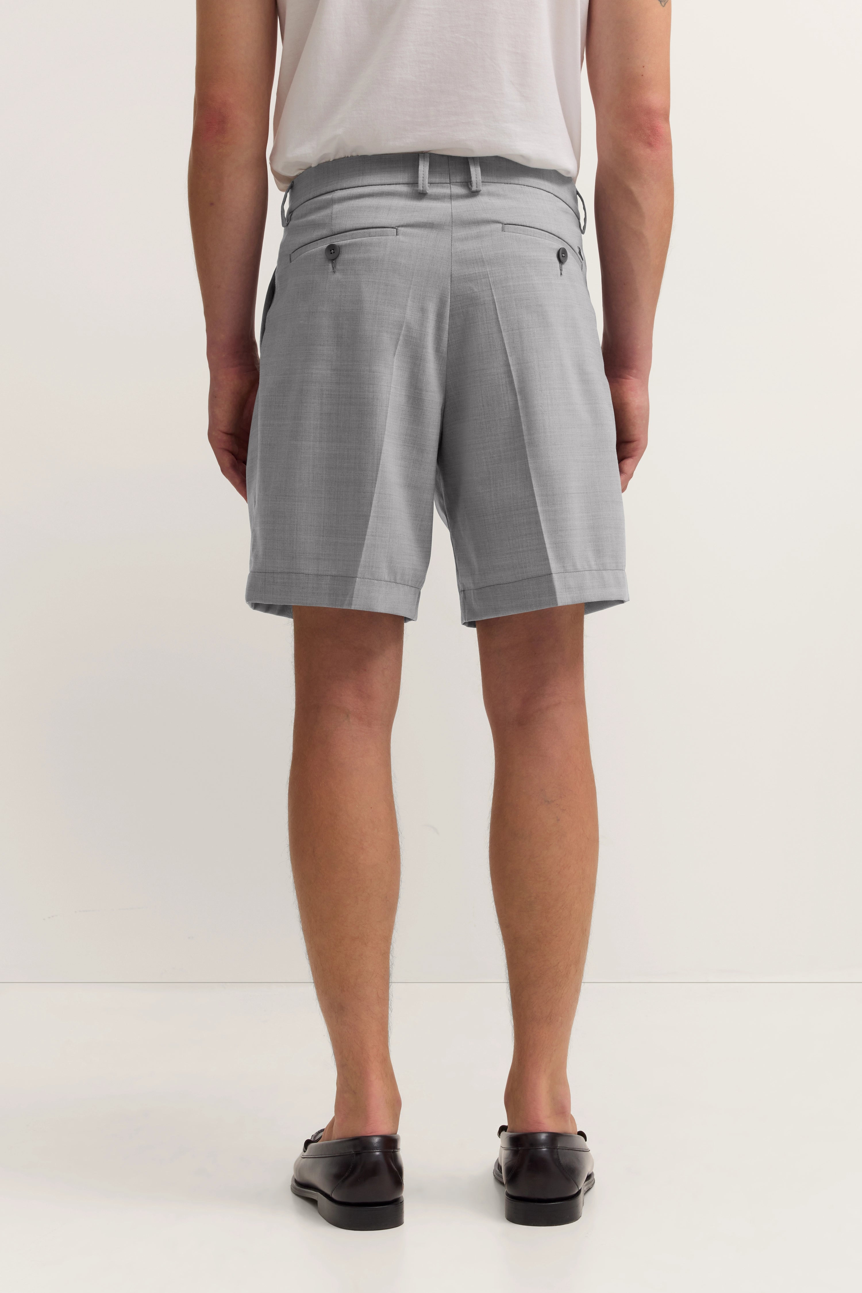 Graue Shorts in Büstenaufnahme, helles T-Shirt, dunkle Schuhe