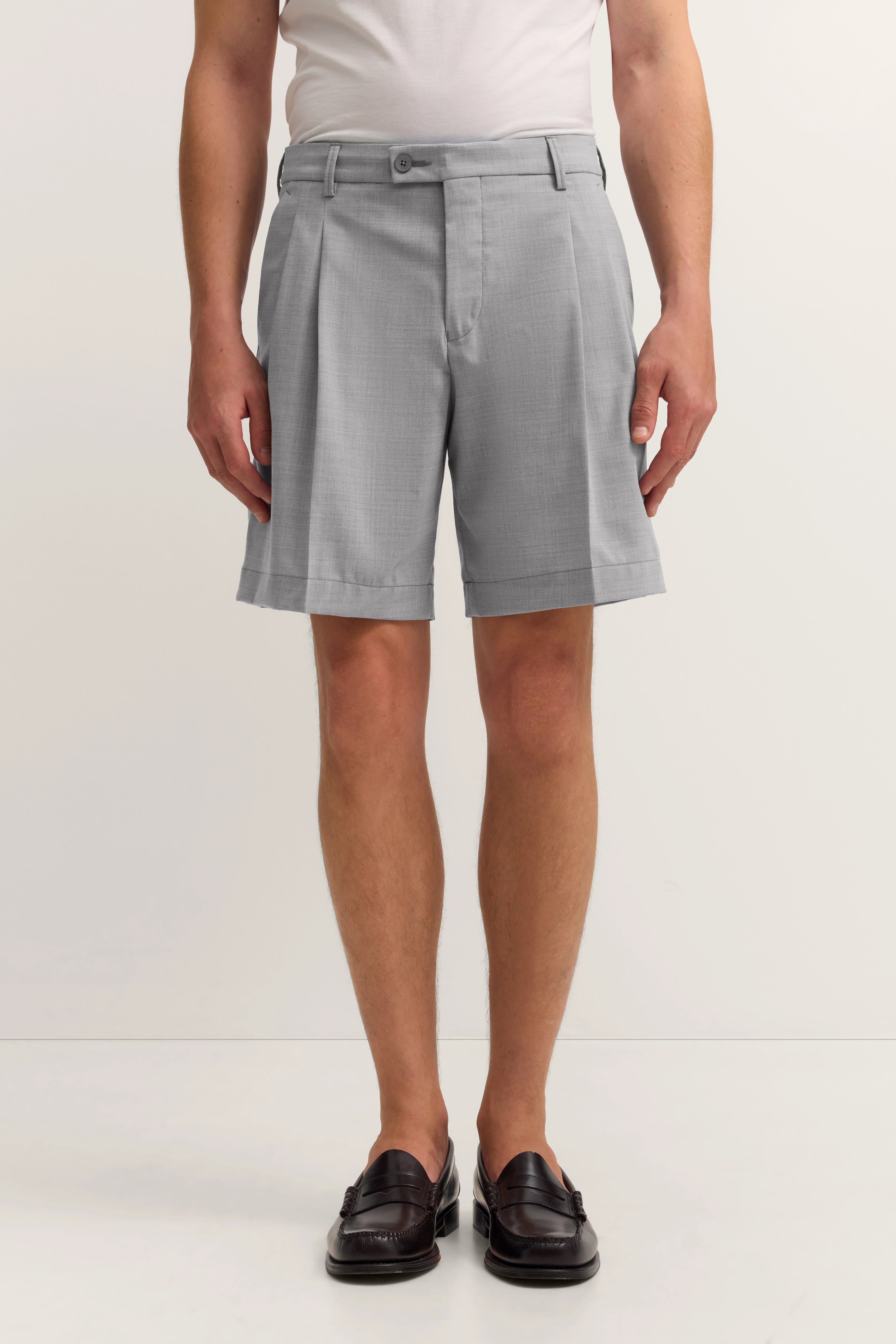 Graue Shorts von bugatti, legeres Modelbild, steht entspannt, kombiniert mit weißen Shirt und eleganten Schuhen.