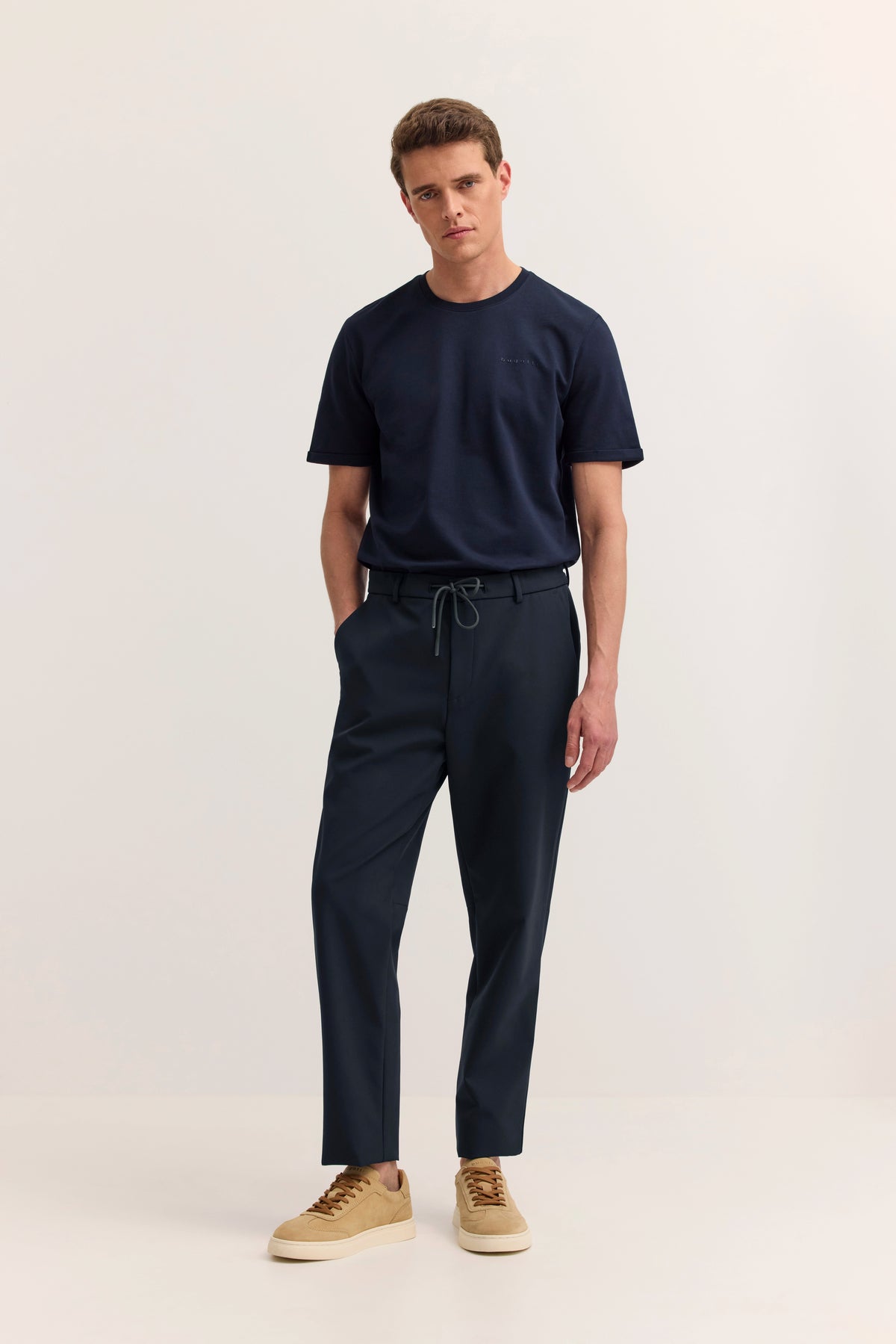 bugatti Model in navy T-Shirt und Hose, beige Sneakers, entspannter Stand, stilvoll und lässig.