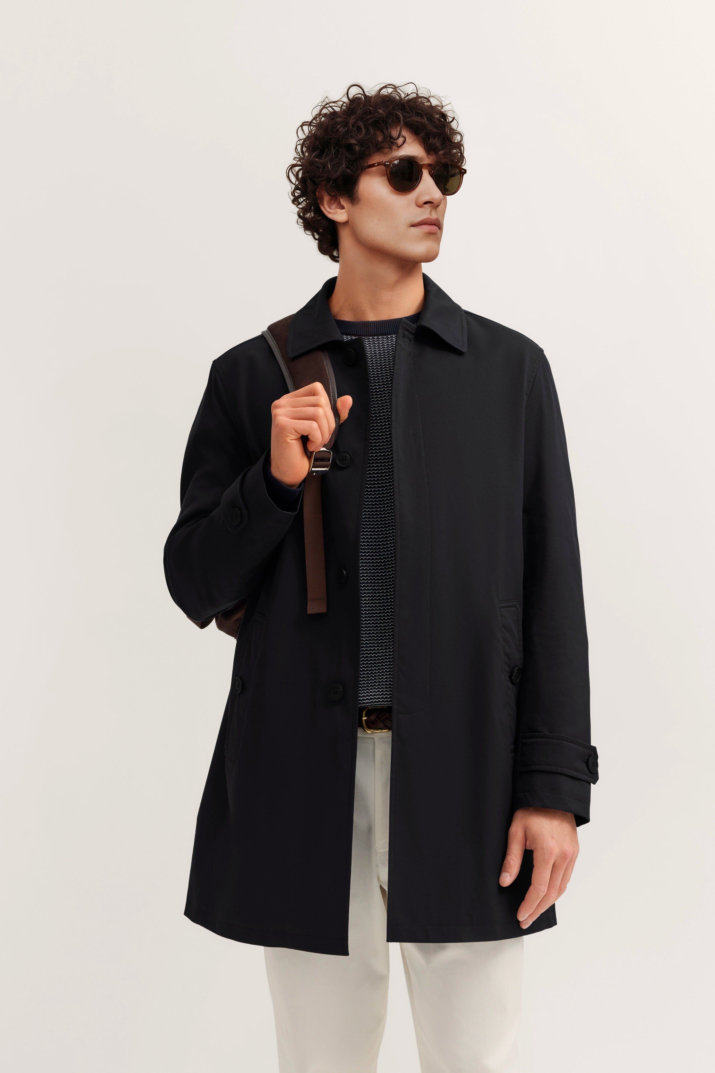 Model in schwarzem bugatti-Mantel, blauem Pullover, weißen Hosen