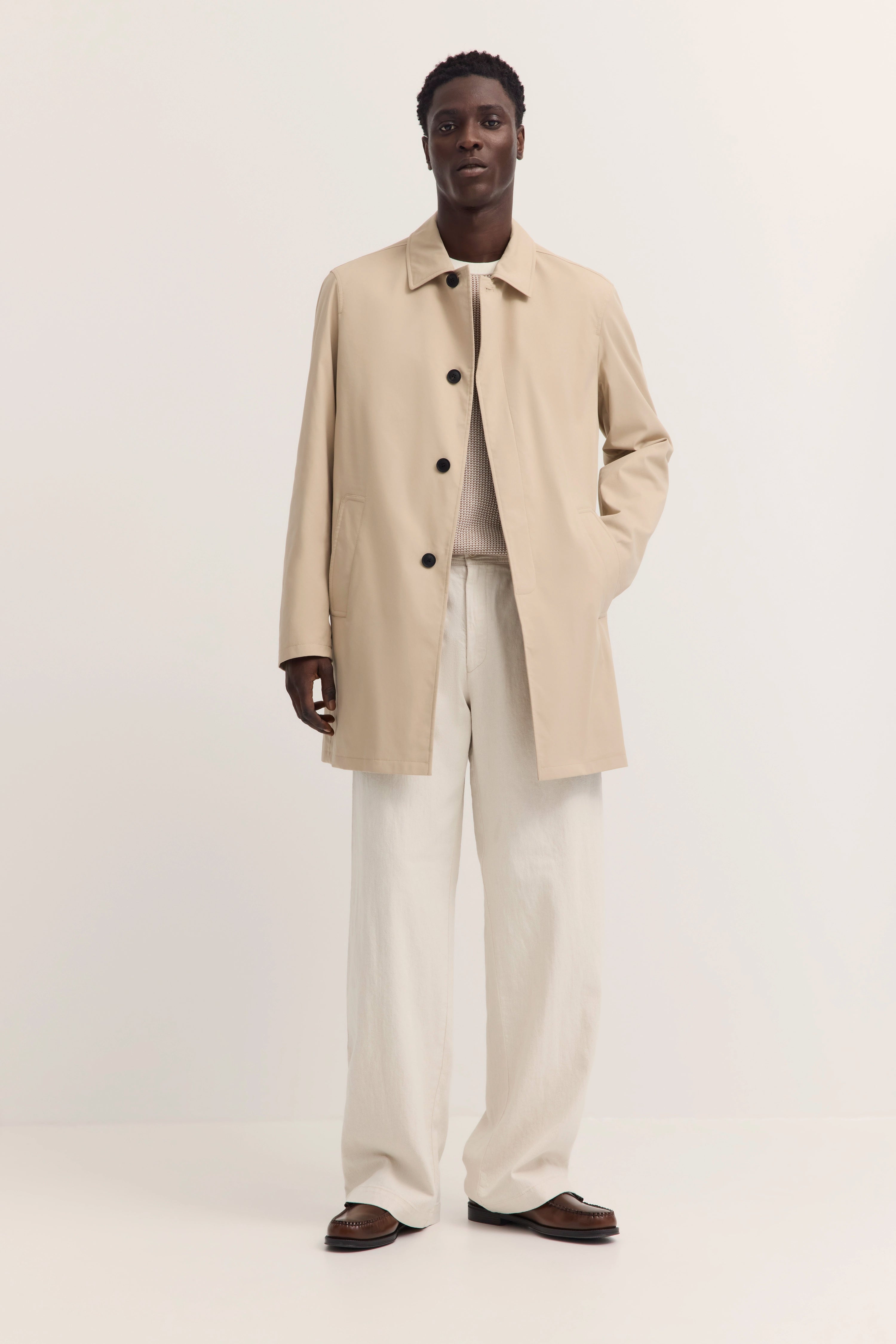 Beiges bugatti Trenchcoat, cremefarbene Hose, legeres Modelbild, entspanntes Posing.