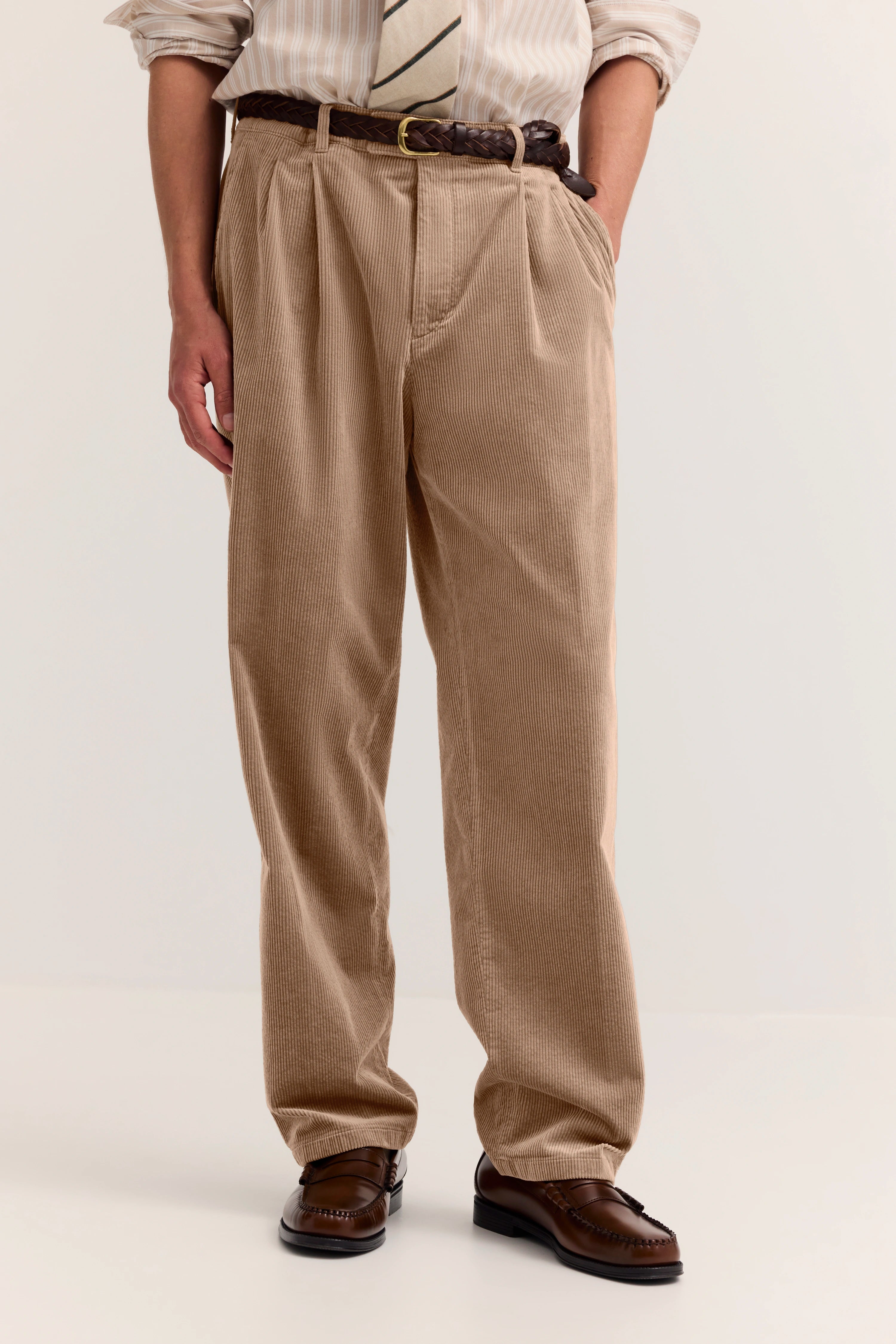 Beige Cordhose mit braunem Gürtel, Hemd und Krawatte, legeres Modelbild, stehend.