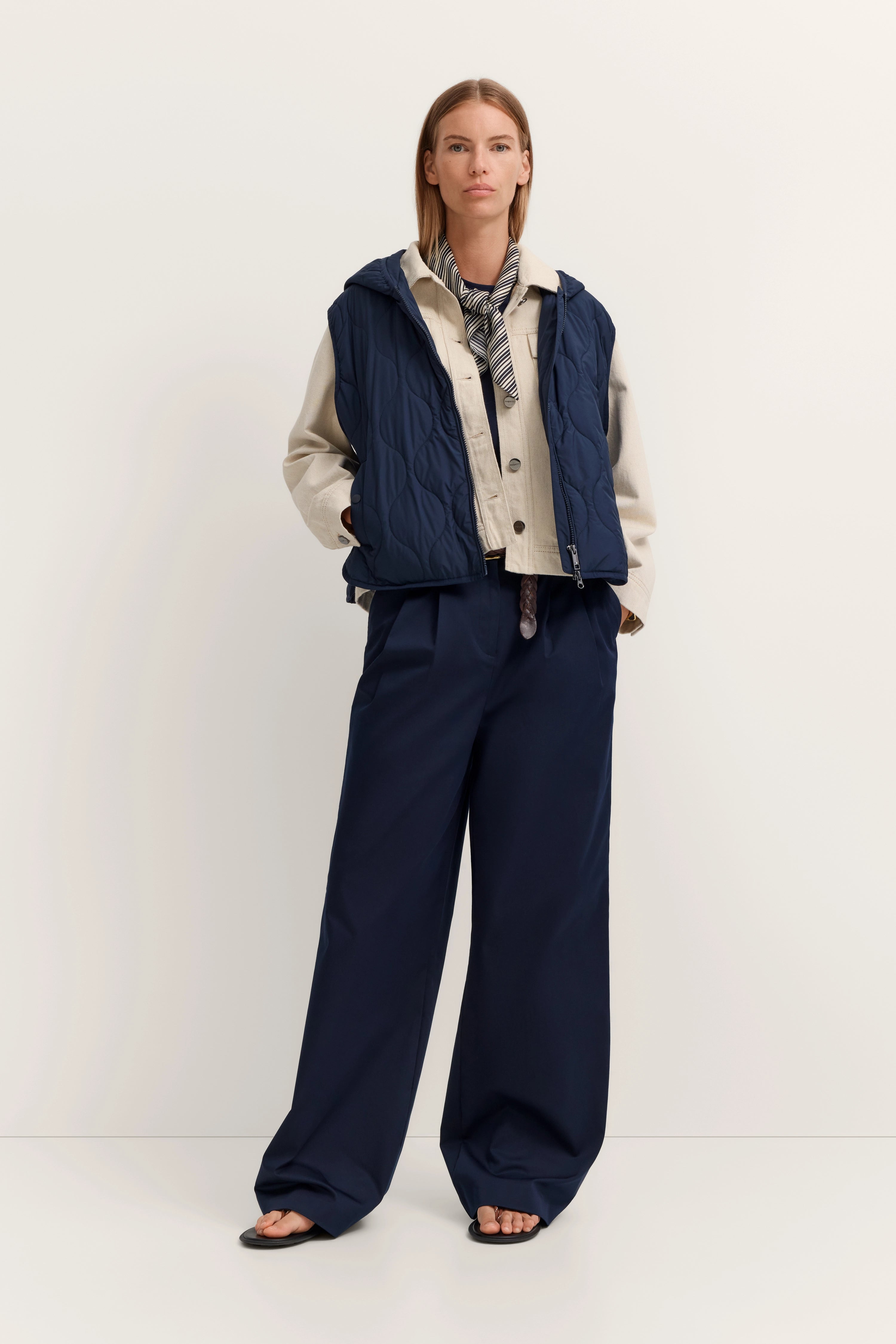 Model in blauem Steppwesten, beige Jacke, blau-weißem Schal und weiten blauen Hosen