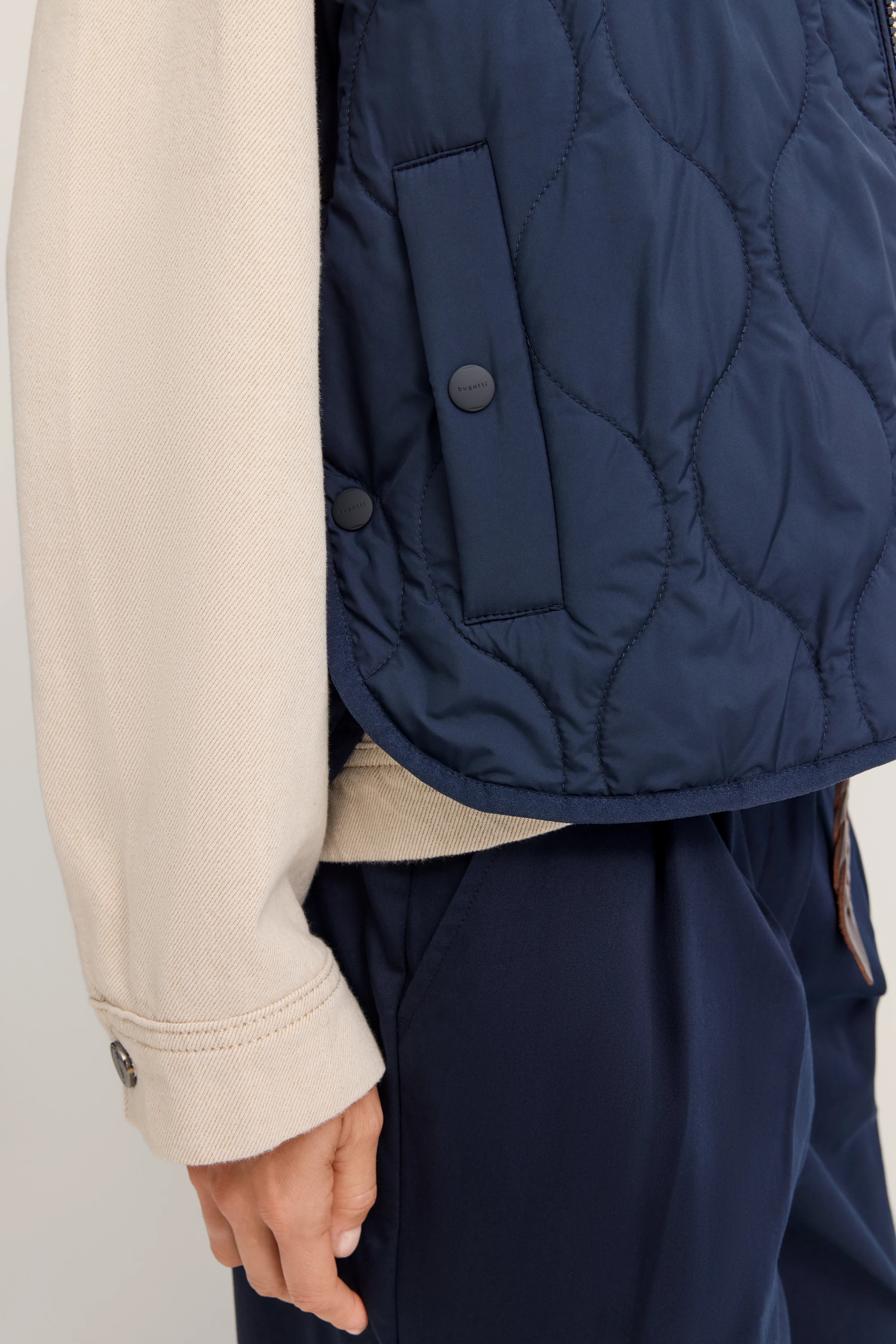 Beige Mantel und blaue gesteppte Weste von bugatti, Detailaufnahme, klassischer Look.