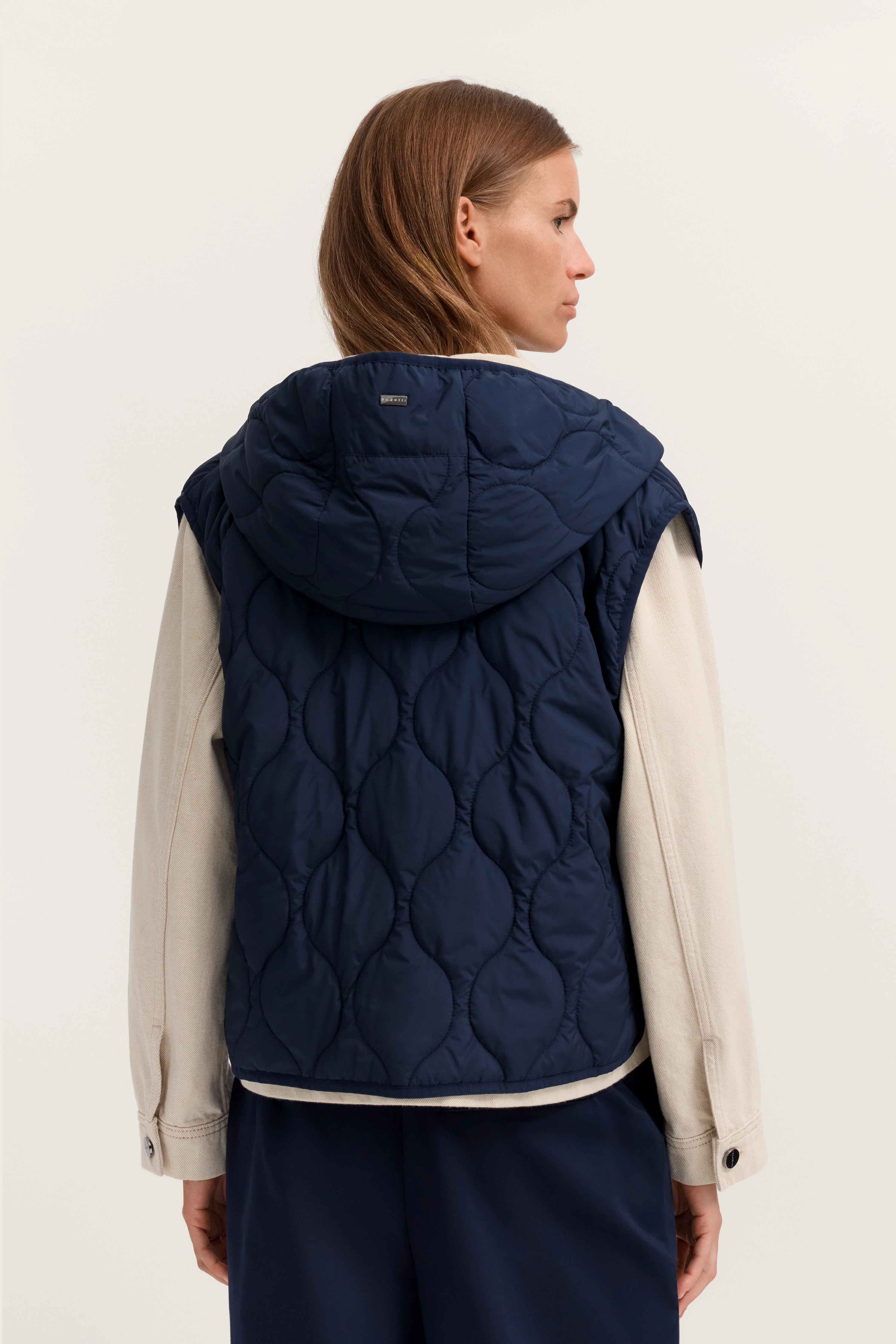 Navy Steppweste von bugatti über cremefarbenem Hemd, Rückansicht, Modell steht entspannt.