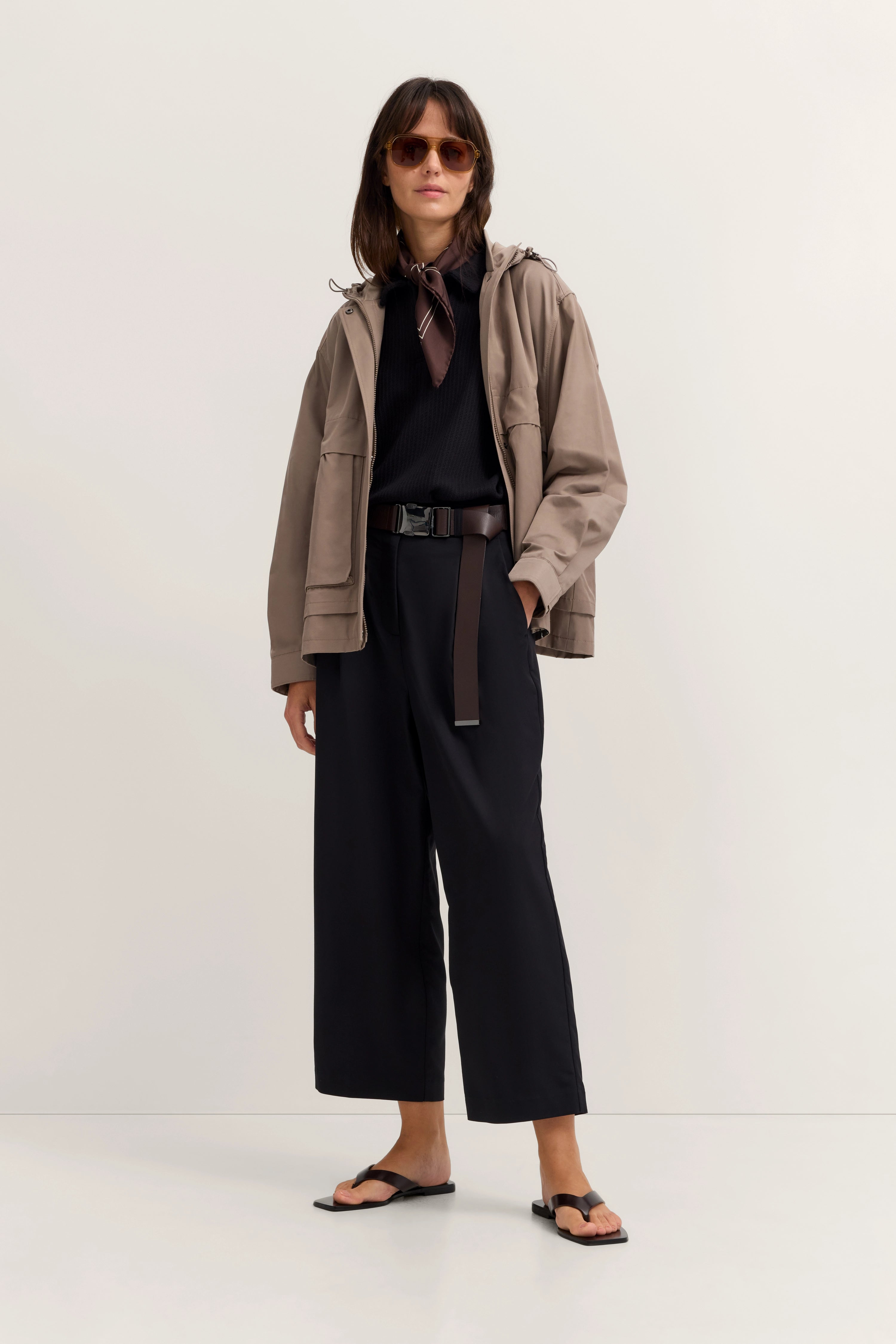Model in beiger Jacke, schwarzem Pullover und Hose. Lockeres Posing, Sonnenbrille. Eleganter bugatti-Stil.