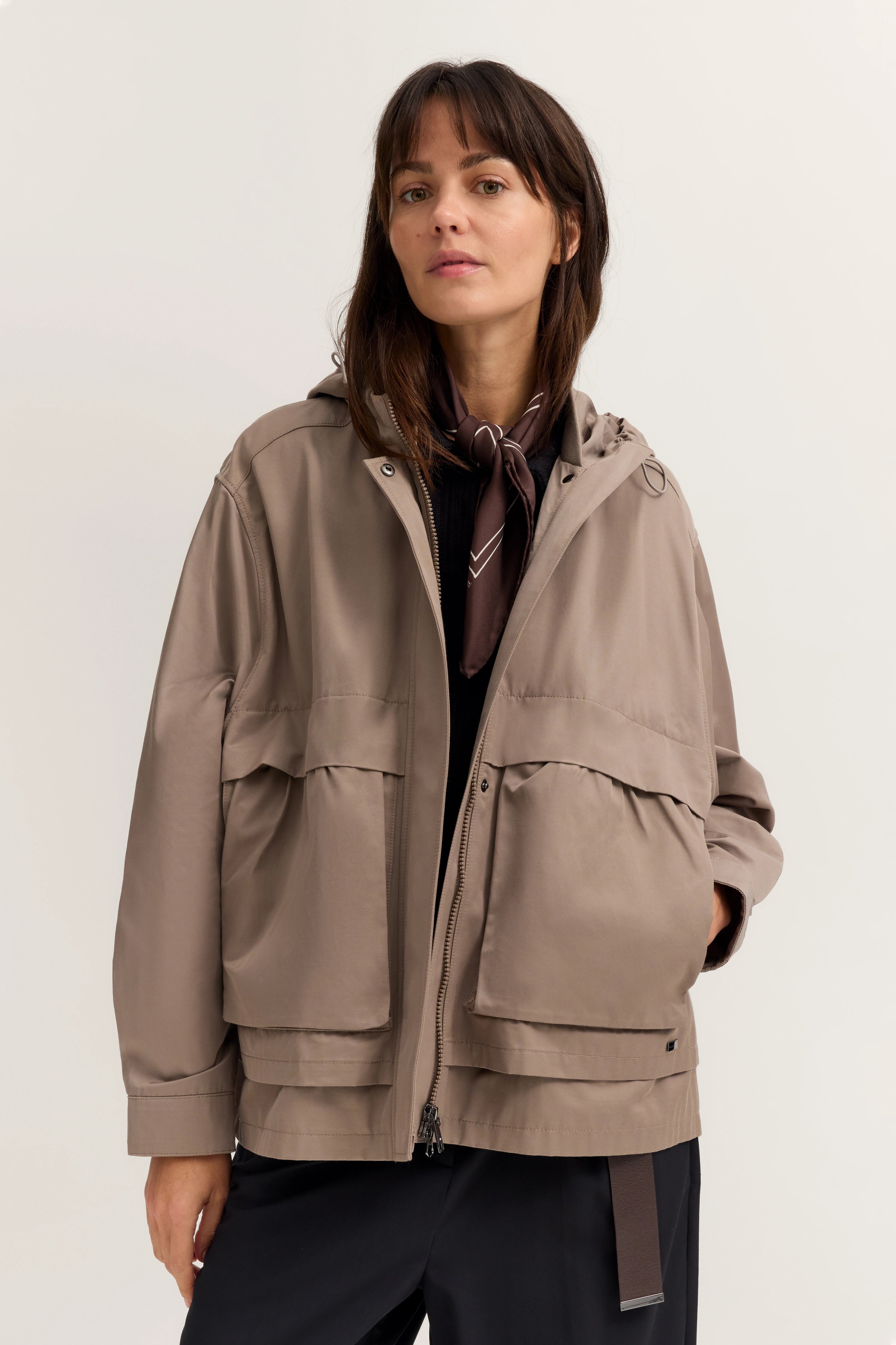 Beige Jacke und schwarze Hose, Modelbild, entspanntes Posing, Schal als Akzent.