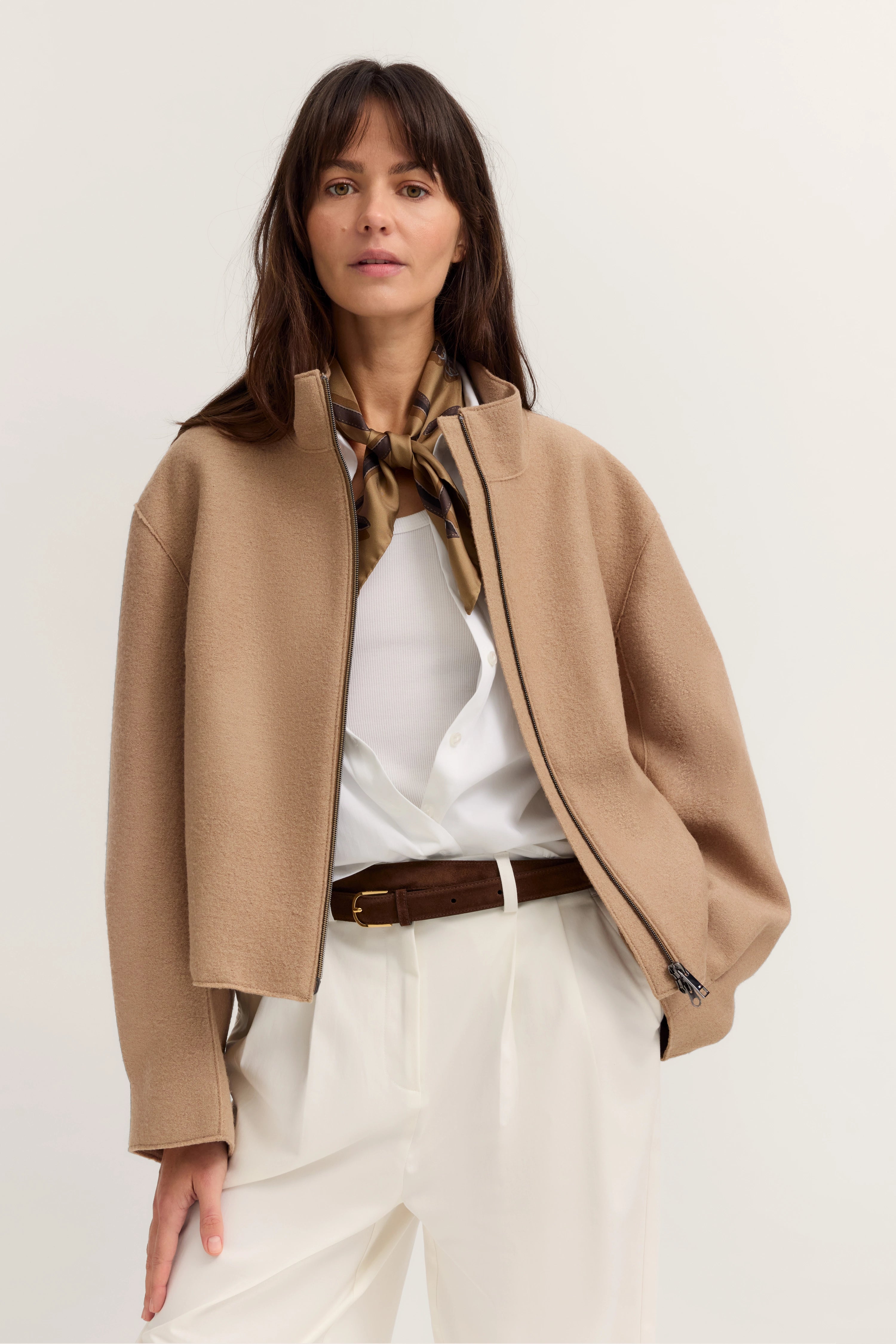 Model in beigem bugatti Blazer, weißer Bluse, braunem Gürtel, eleganter Pose.