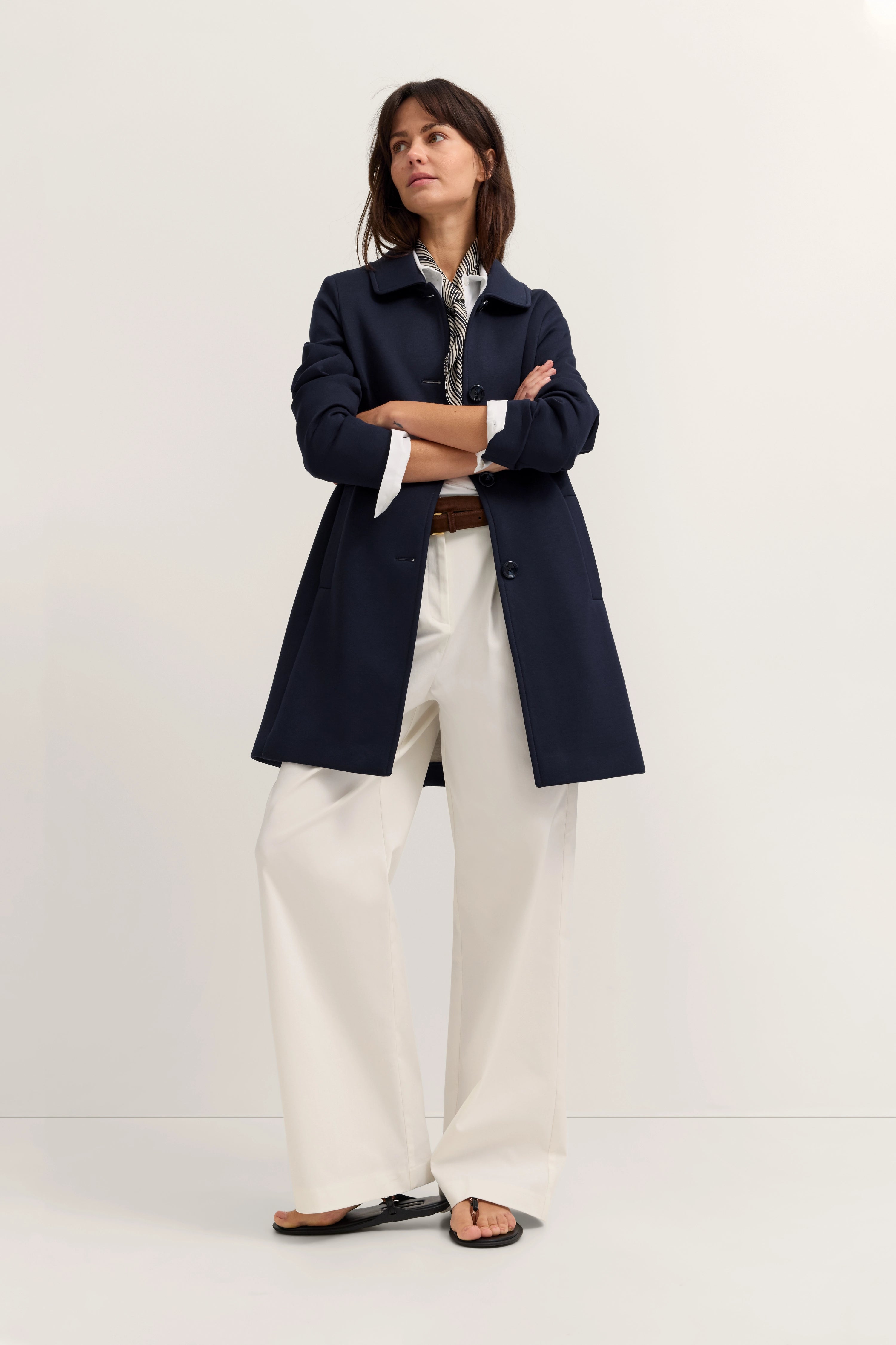 Model in marineblauem Mantel, weißer Hose, Posing mit verschränkten Armen. Eleganter bugatti Stil.