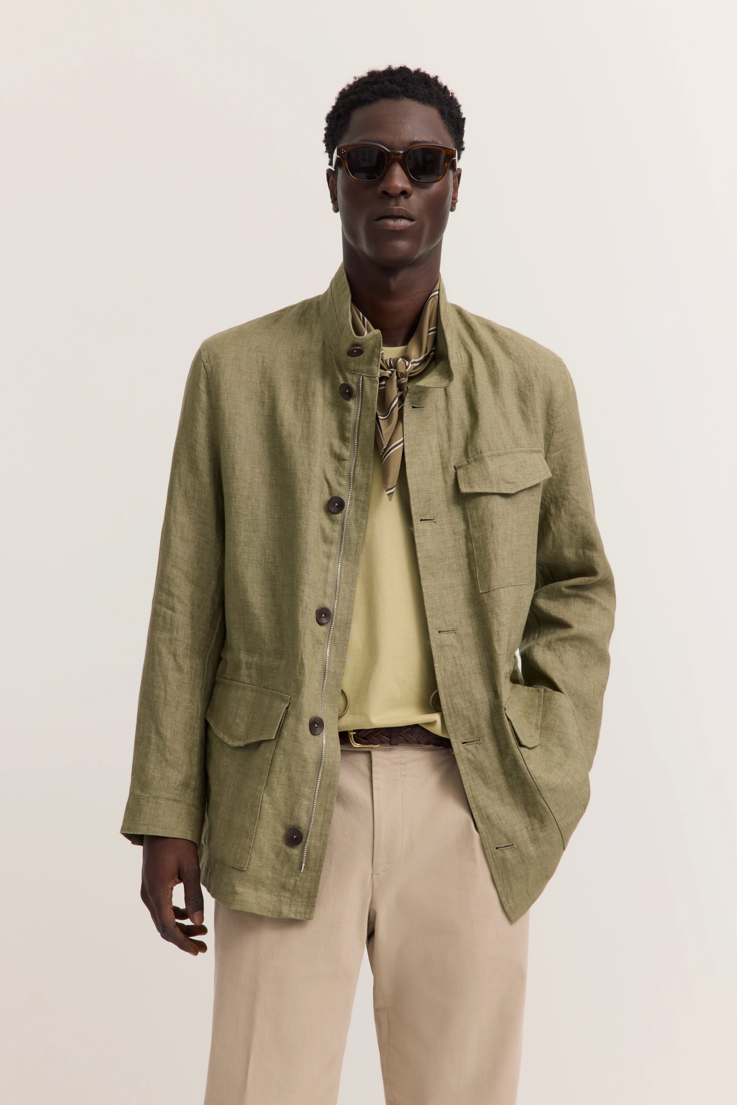 bugatti Modelbild: Olive Jacke, beiges Shirt, beige Hose, legeres Posing, Sonnenbrille.