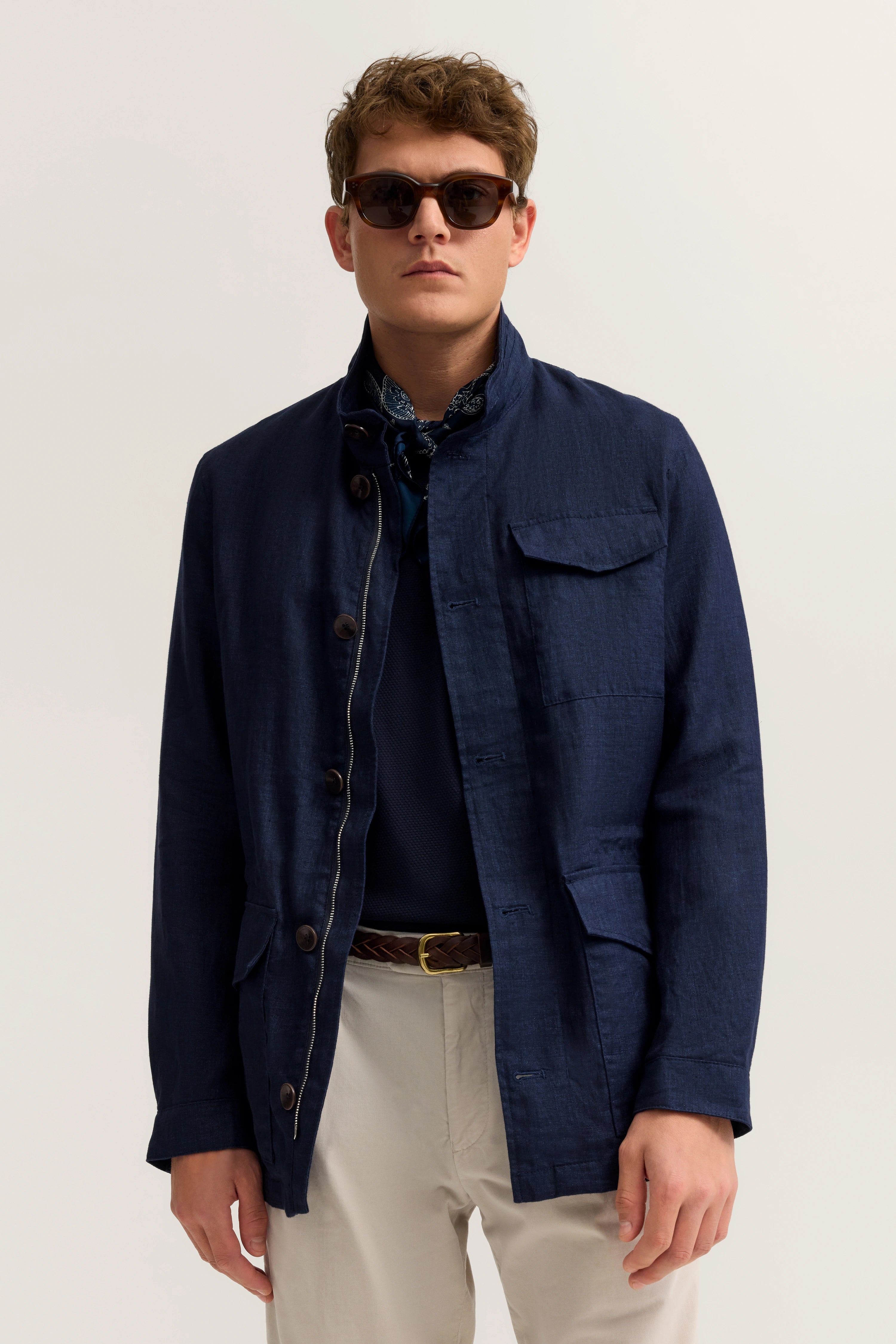 Model in marineblauer bugatti Jacke, beige Hose, Sonnenbrille. Lässig-elegante Pose.
