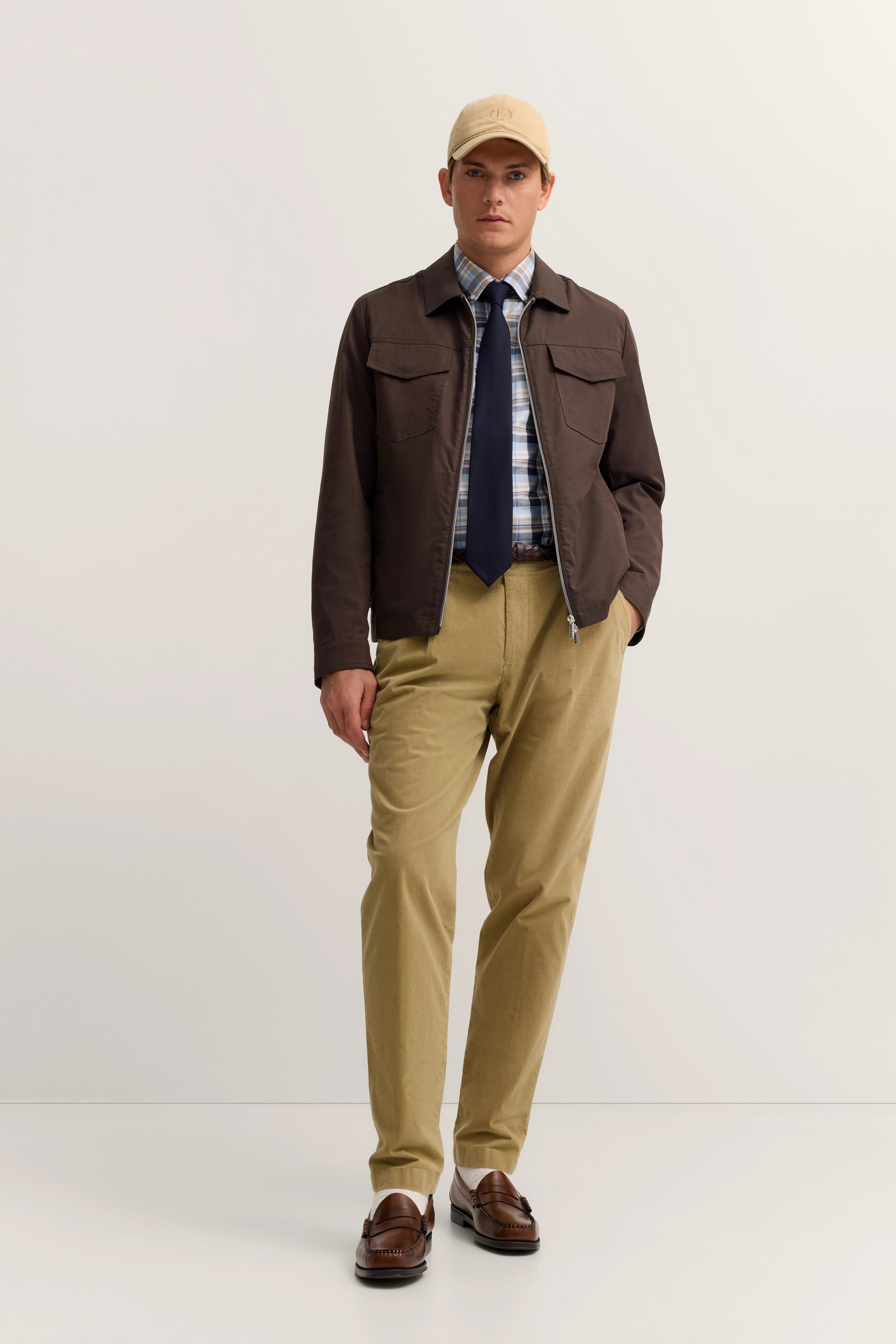 Model in brauner Jacke, kariertem Hemd, blauer Krawatte und beigefarbener Hose, frontal stehend.