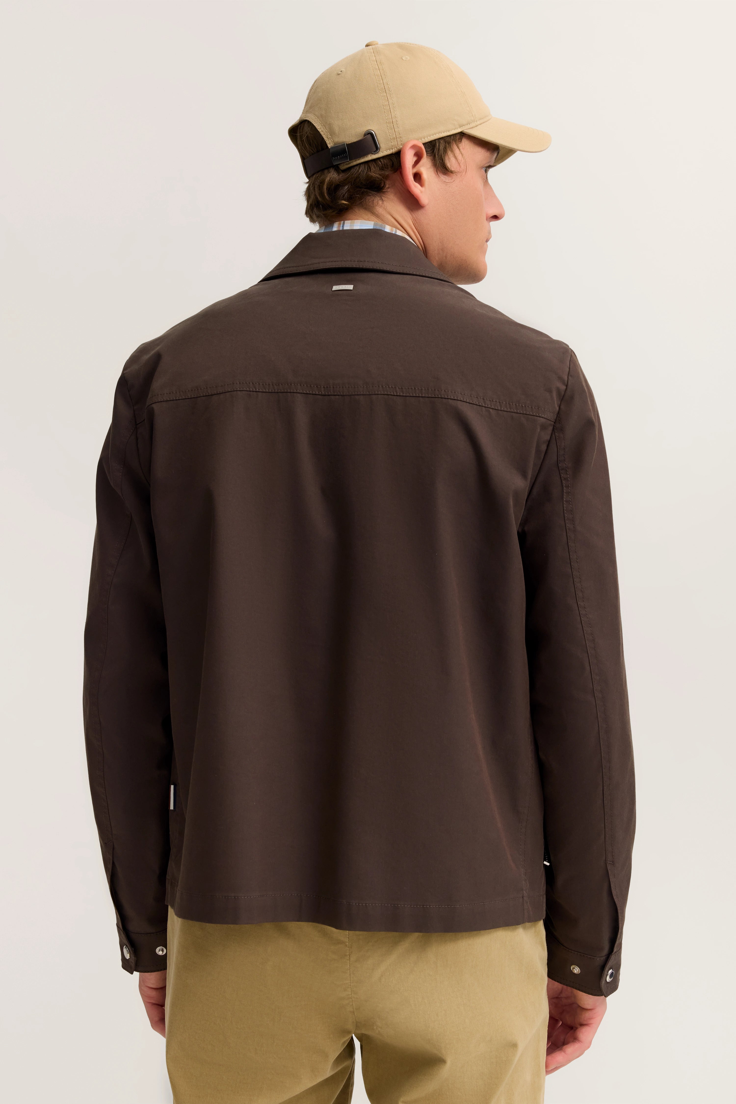 Braune Jacke und beige Hose, Rückansicht, leger, mit beigefarbener Kappe, bugatti Stil.