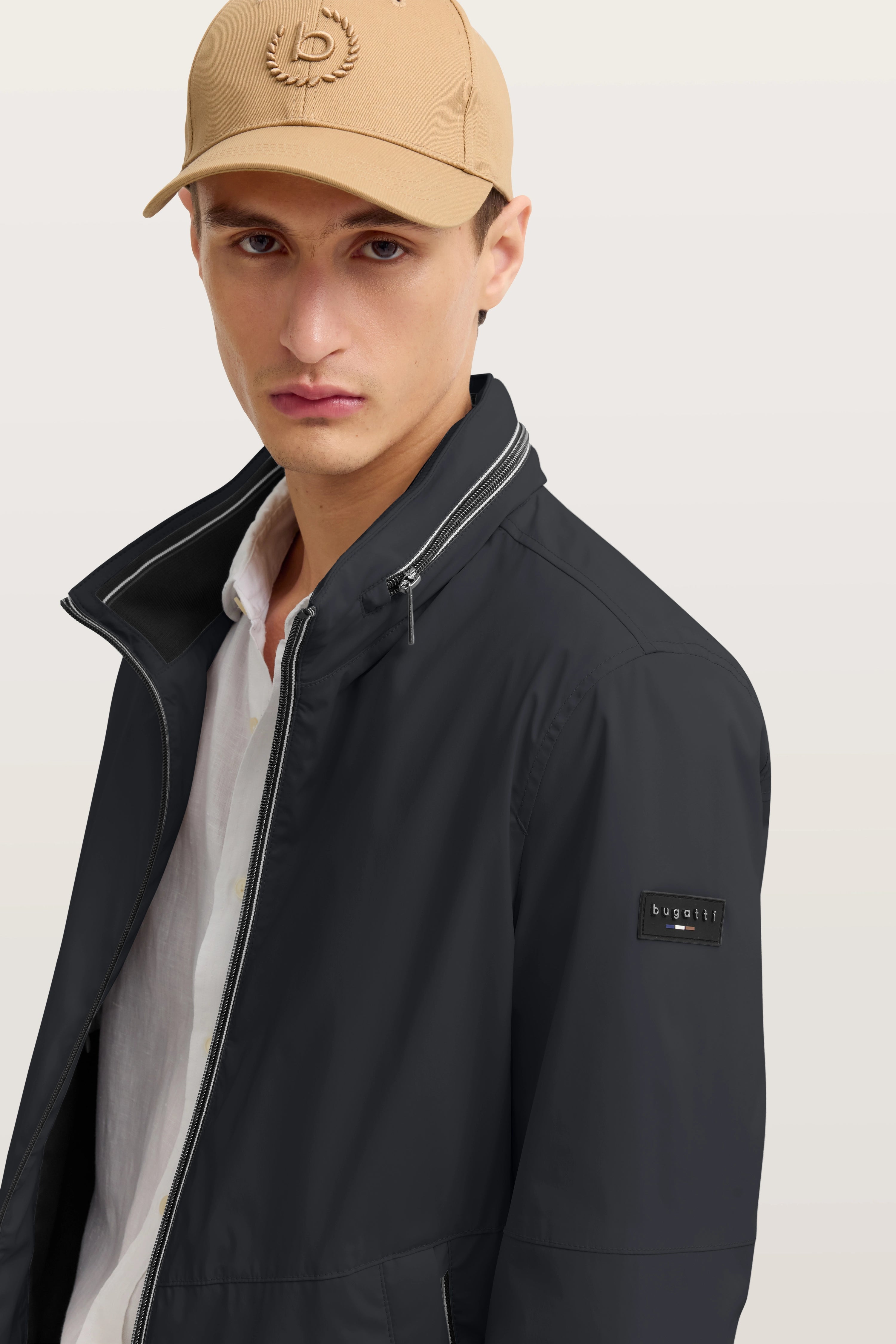 Model in schwarzer bugatti-Jacke, beige Kappe, weißes Hemd, lässiger Look.