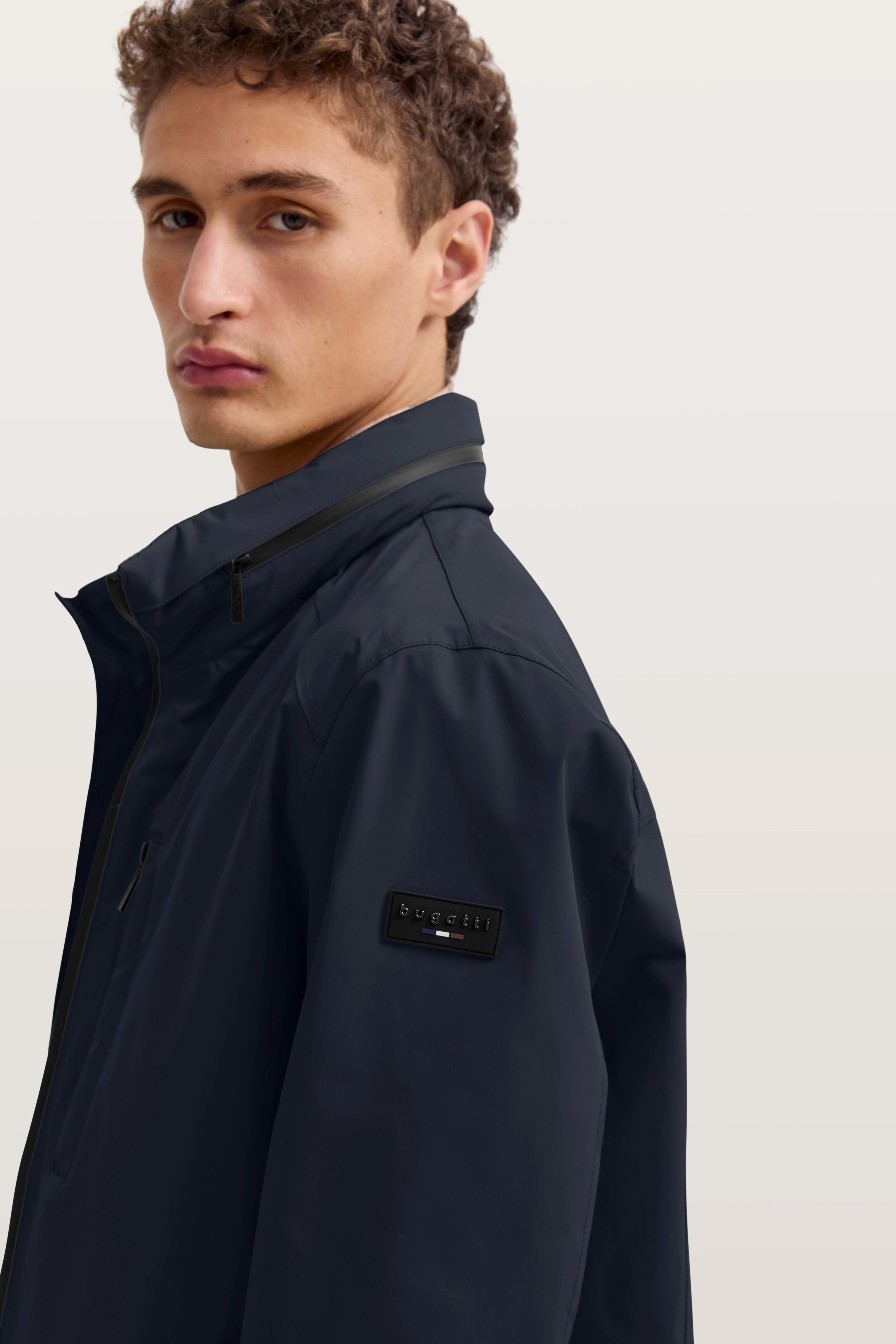 Dunkelblaue bugatti Jacke auf Model, Rückansicht, entspanntes Posing, kombiniert mit weißer Hose.