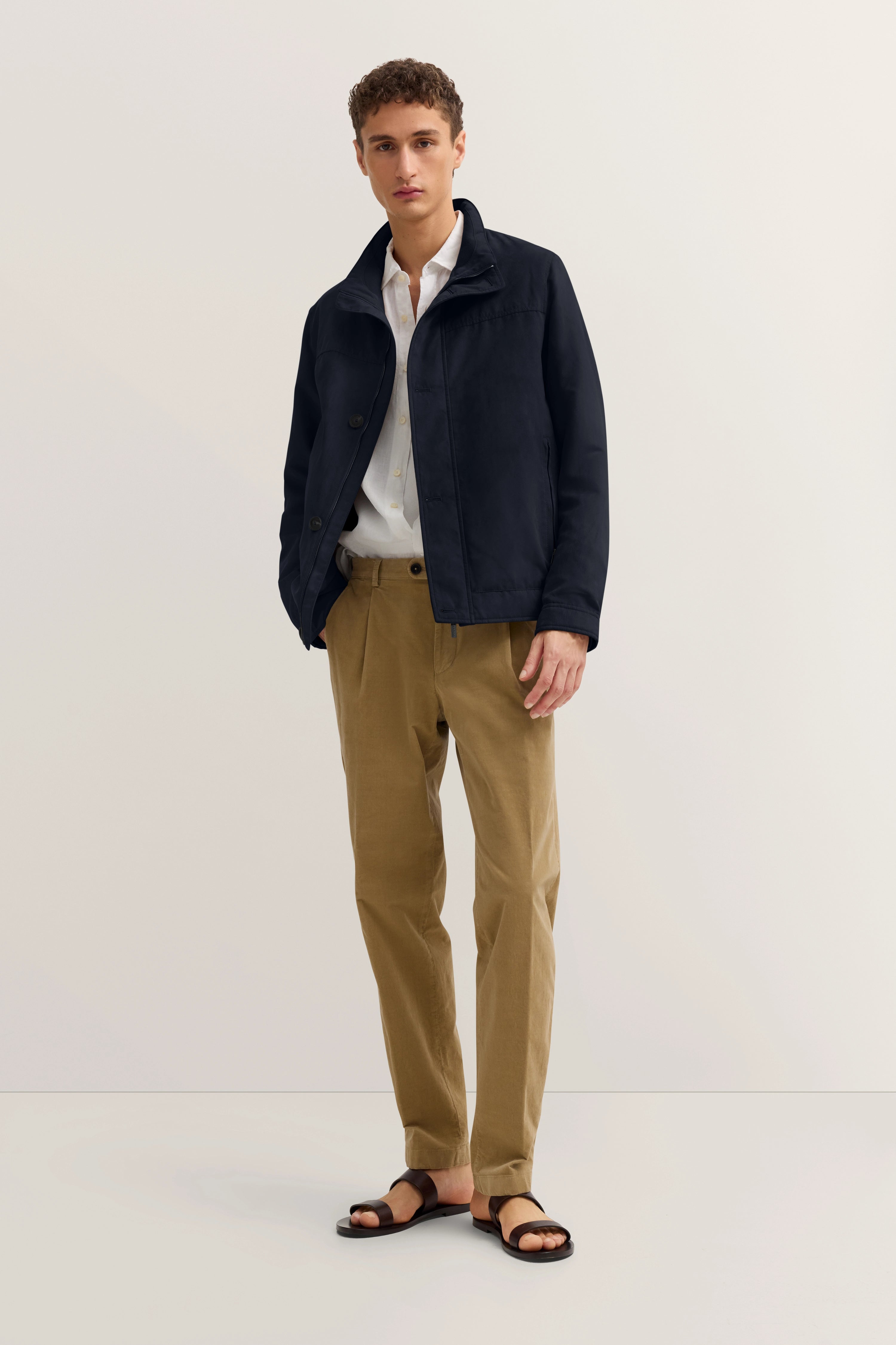 Model in legerem Outfit mit marineblauer Jacke, weißem Hemd und beigen Hosen von bugatti.