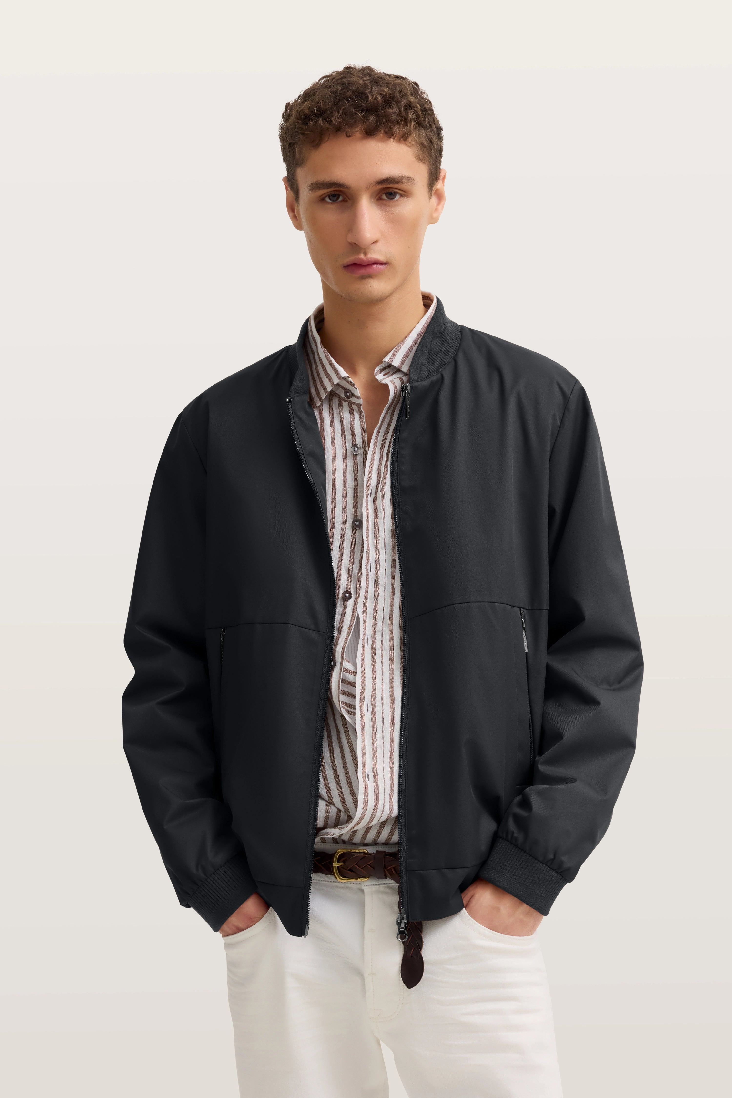 bugatti Modelbild, schwarzer Blouson, gestreiftes Hemd, weiße Hose, entspannte Pose.