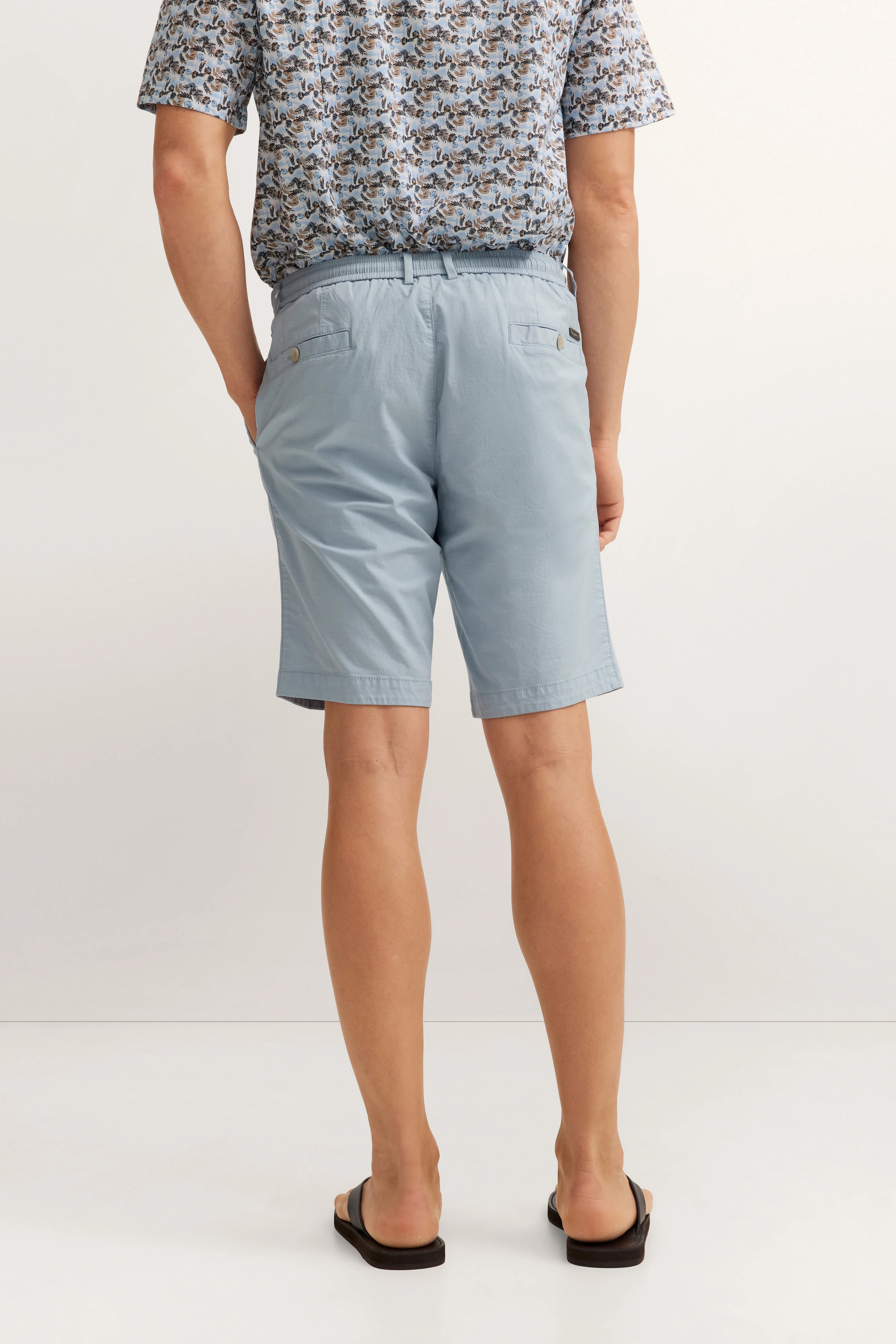 Blaues Hemd mit Muster und hellblaue Shorts, Model von hinten stehend, lässiger Look.