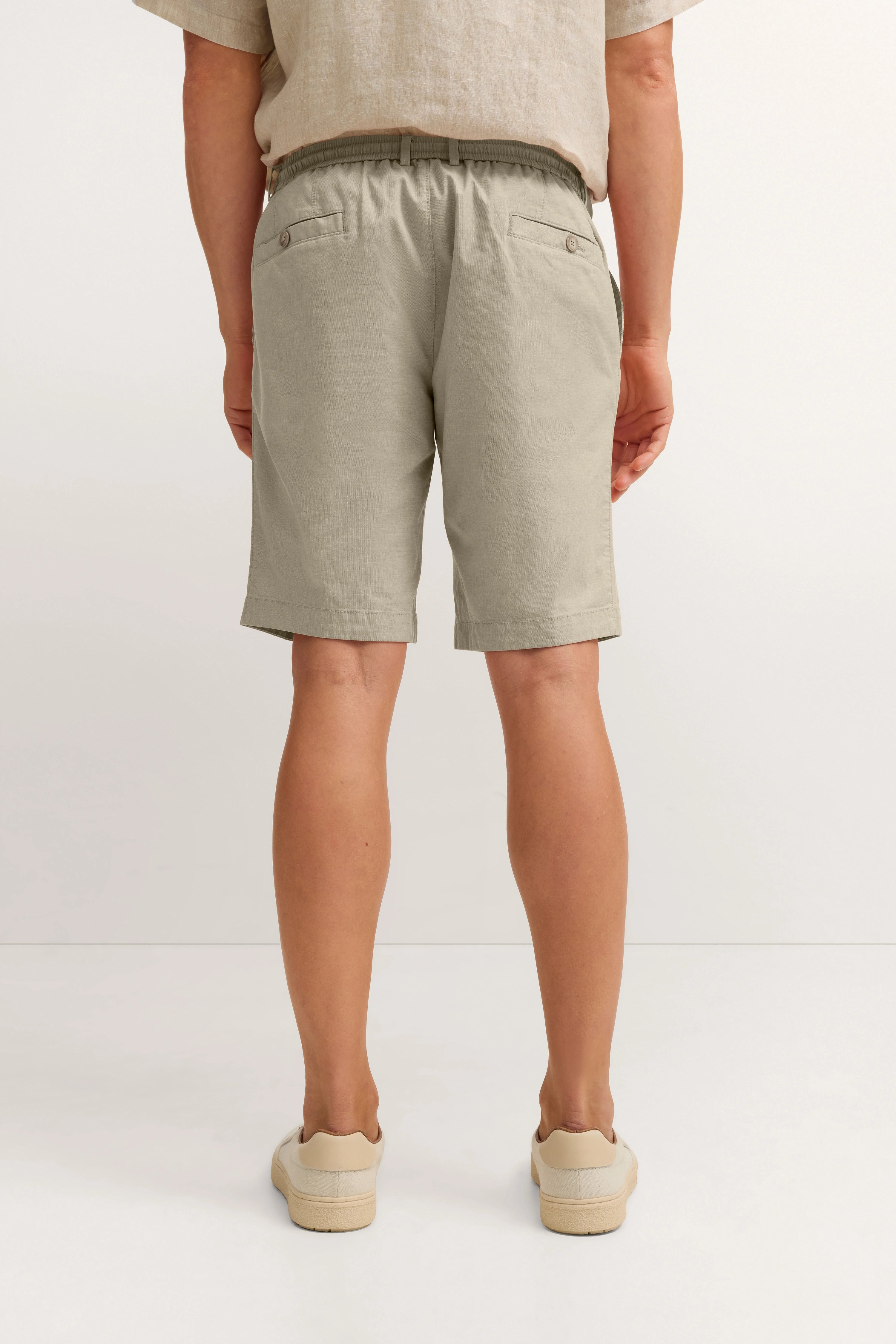 Beiger Leinenlook mit Shorts und Sneakers, legeres Modelbild von hinten, entspannte Pose.