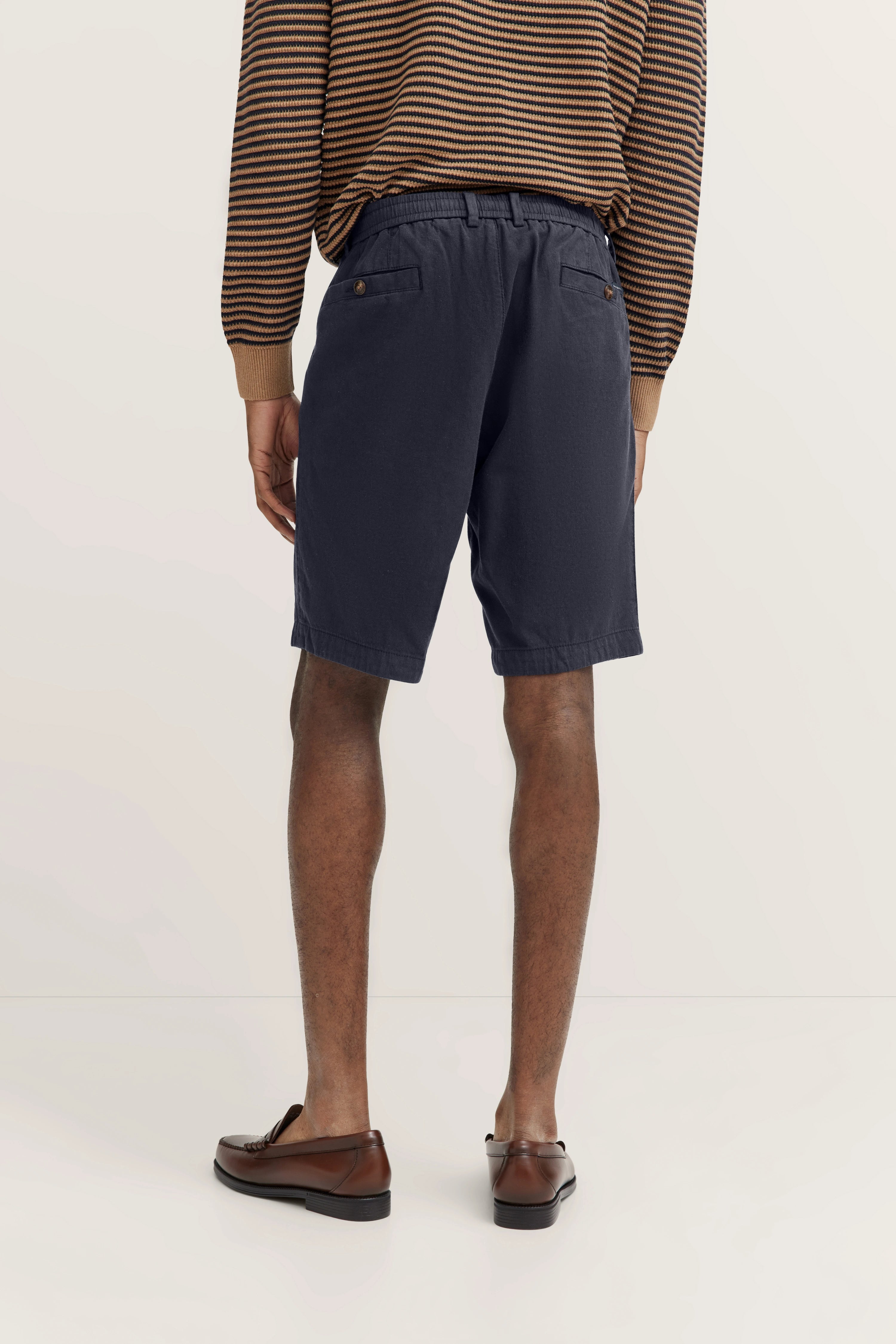 Streifenpullover und dunkelblaue Shorts, legeres Modelbild von hinten, braune Schuhe.