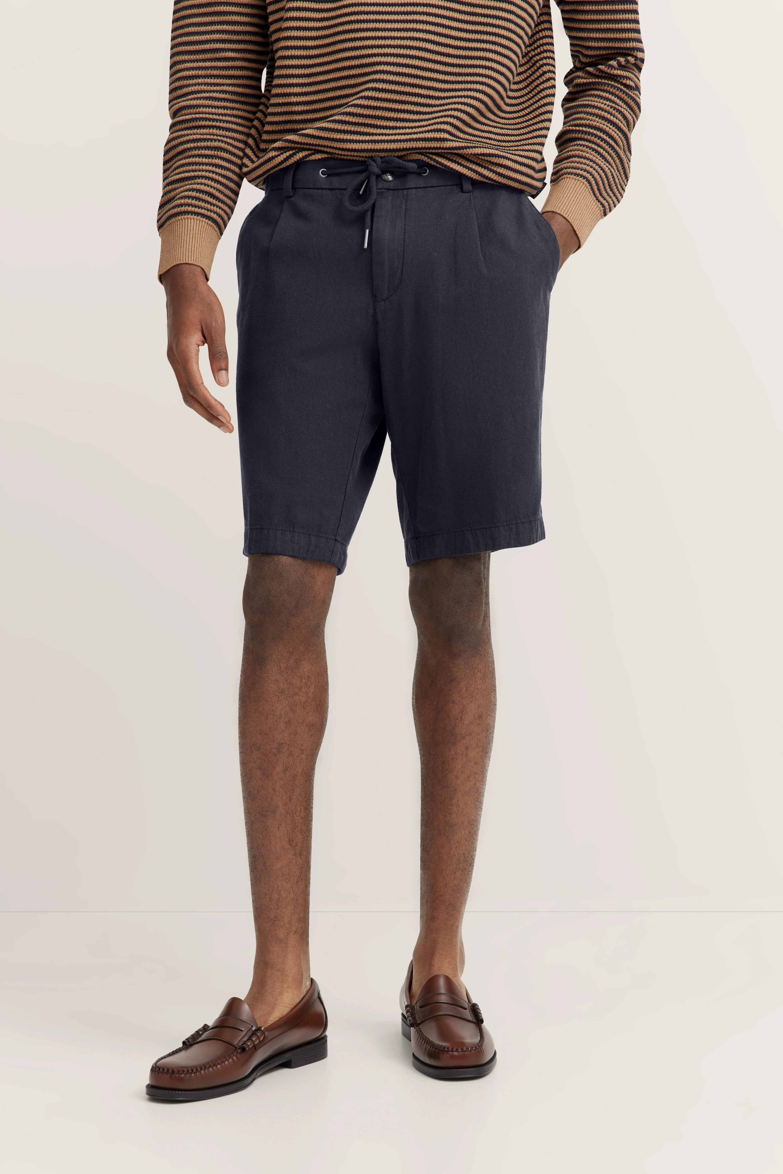 Streifenpullover in Braun mit dunkelblauer Shorts und braunen Loafern, Modelbild, entspannte Haltung.