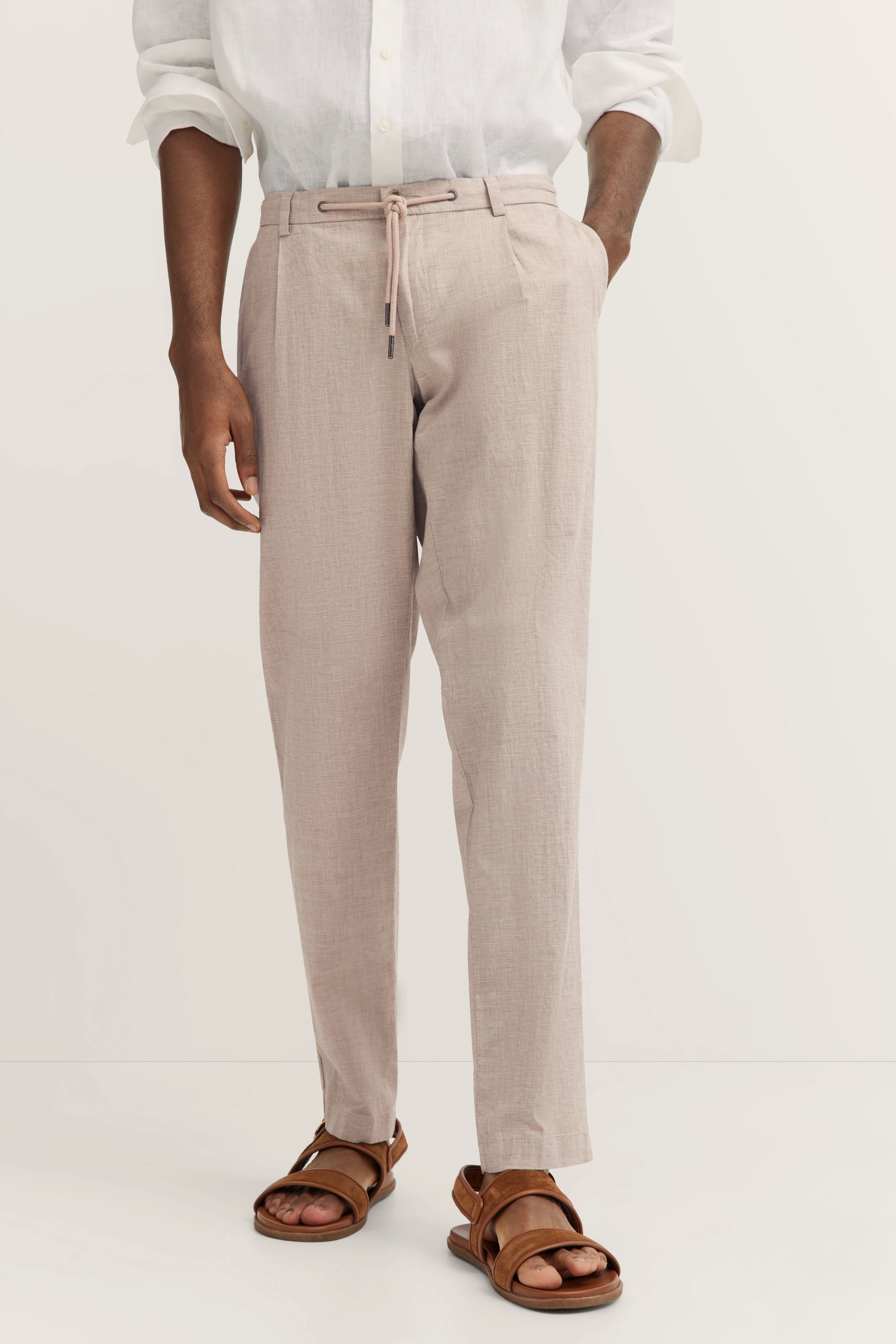 Beige Hose mit weißem Leinenhemd und braunen Sandalen, legeres Modelbild.