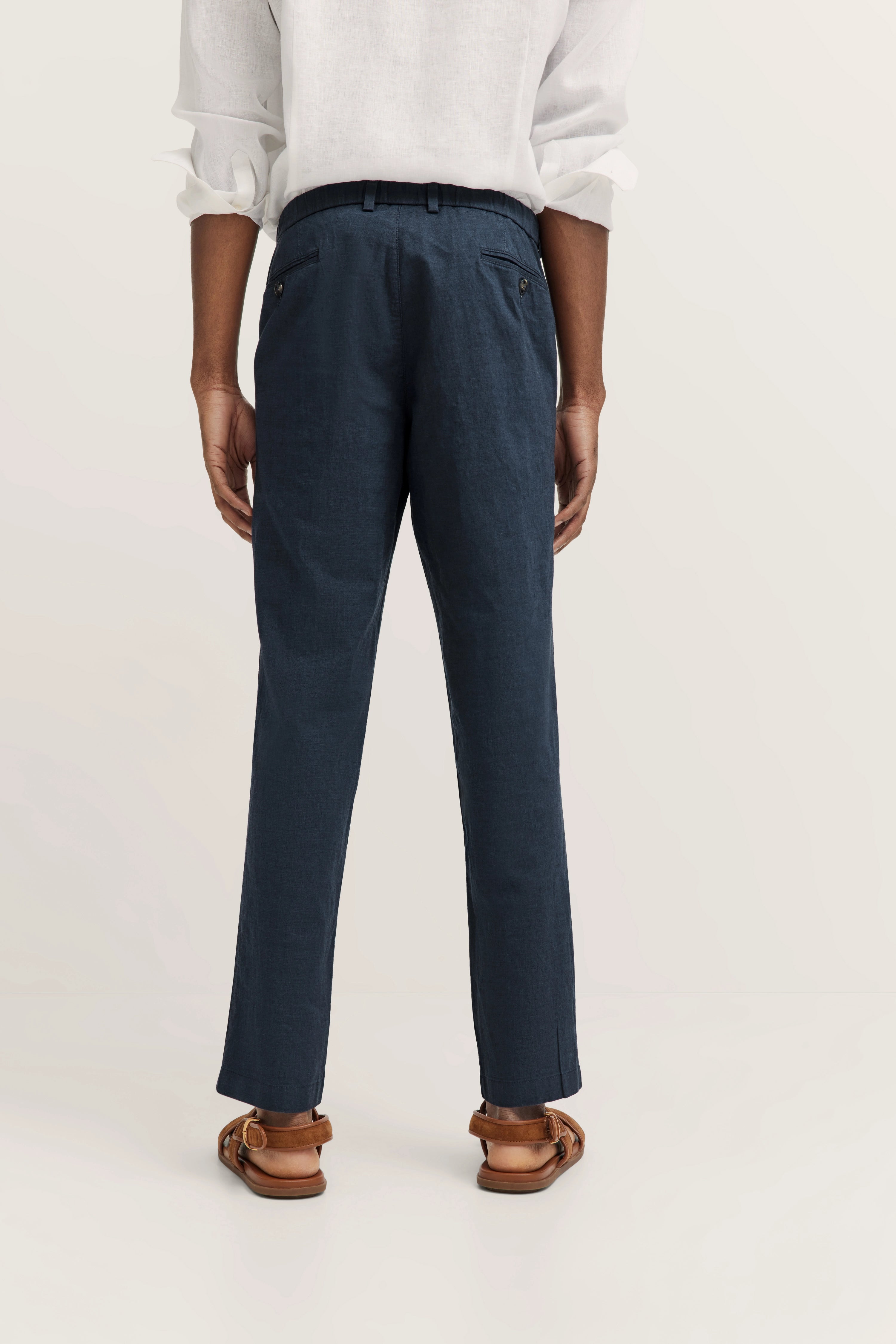 Rückansicht: Weißes Hemd, blaue Hose, braune Sandalen. Legeres Modelbild, entspannte Haltung.