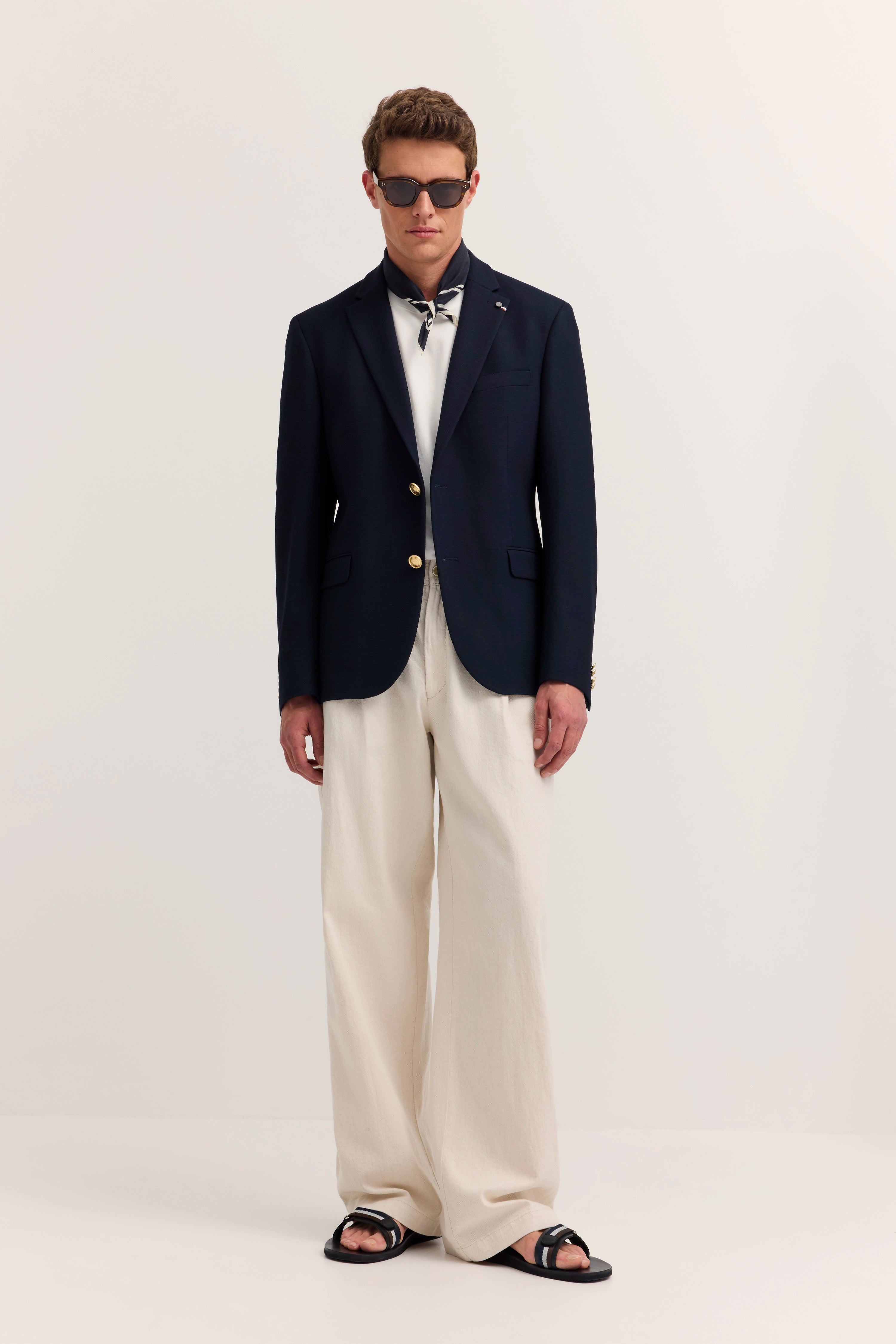 Model in navy Blazer, weißem Shirt, beigen Hosen und Sandalen. Posing: Entspannt, frontal stehend.