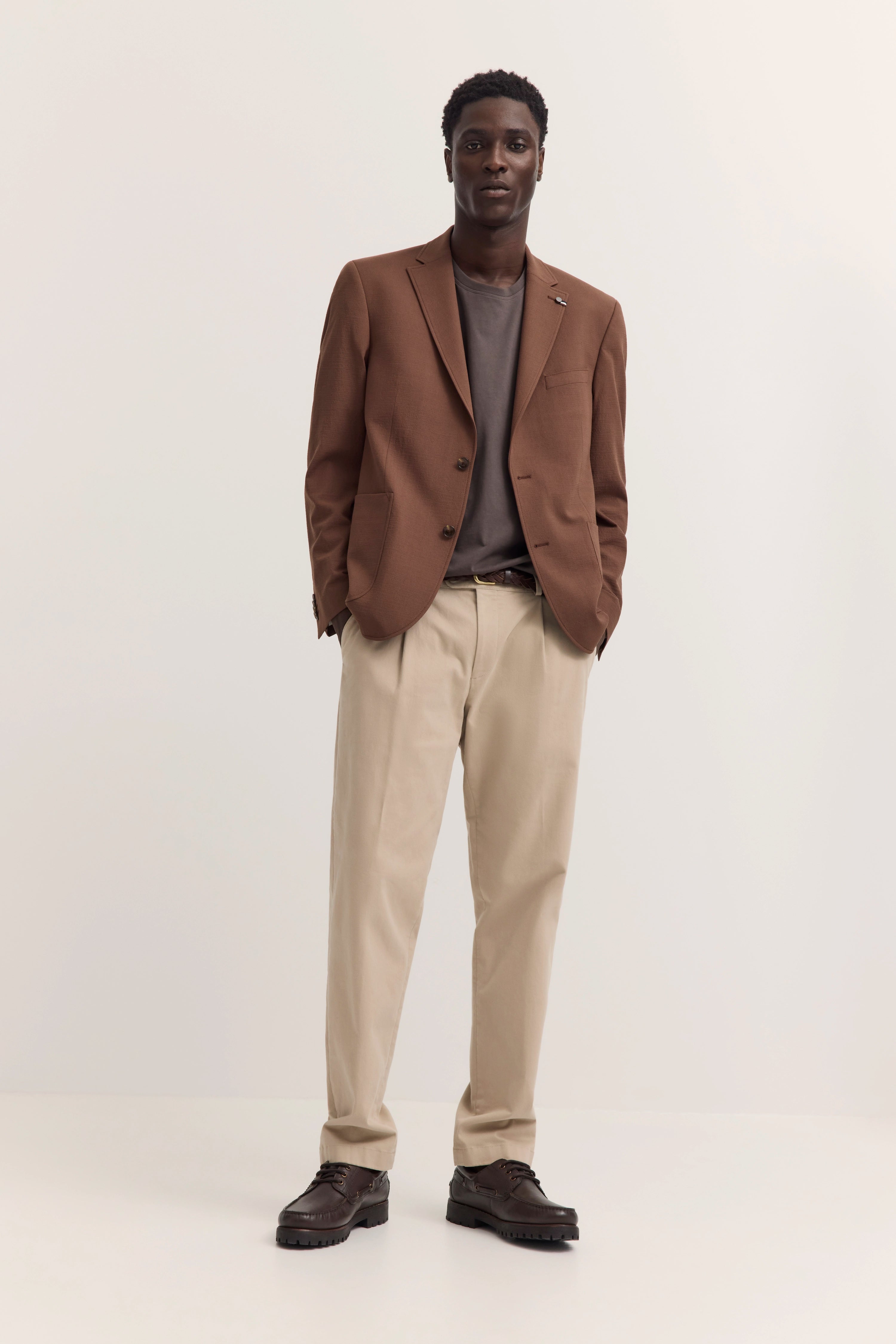 Brauner bugatti-Blazer, graues Shirt, beige Chinos, braune Schuhe. Model steht entspannt.