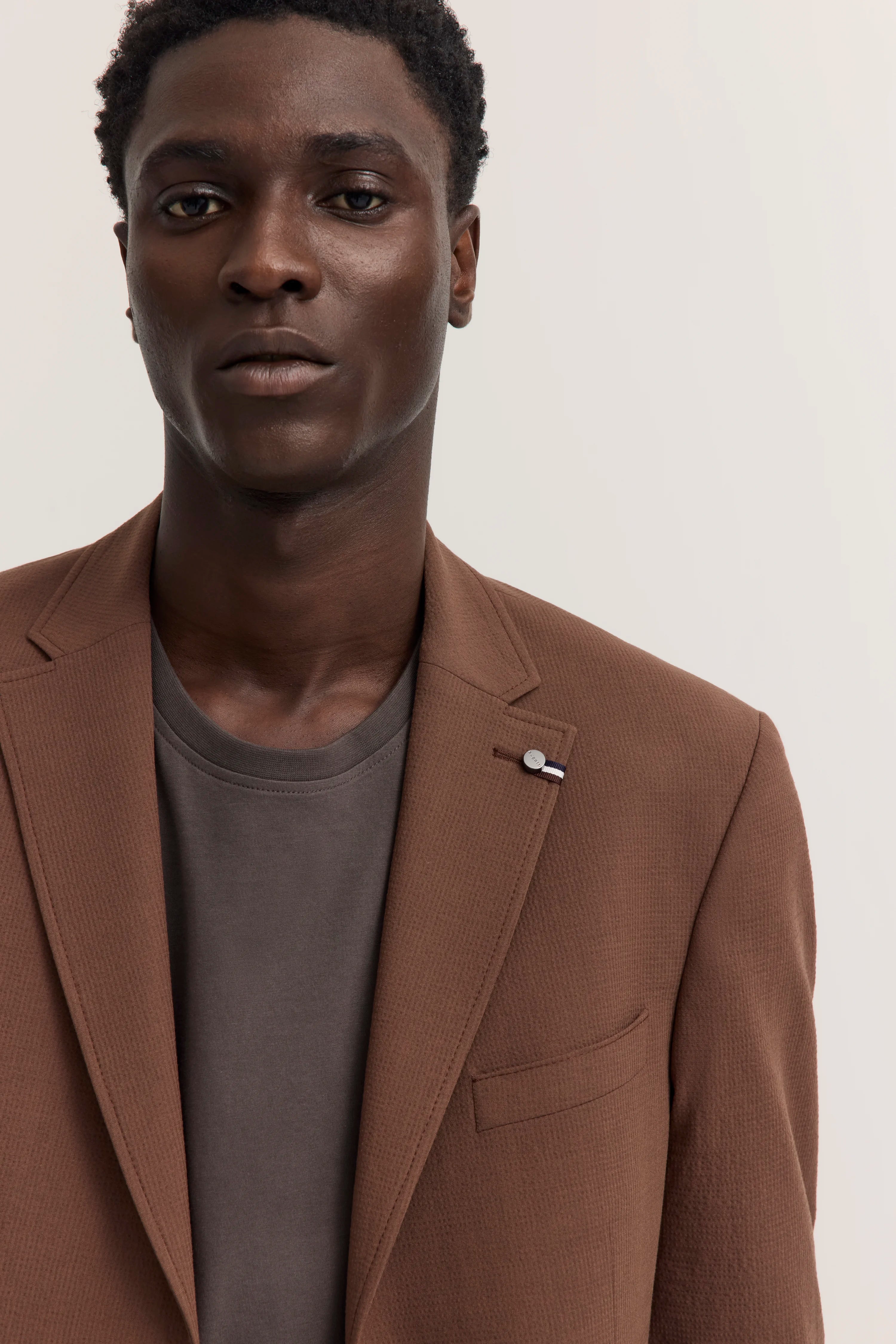 Büstenbild von Mann mit braunem bugatti-Blazer und grauem Shirt, lässiger Stil.