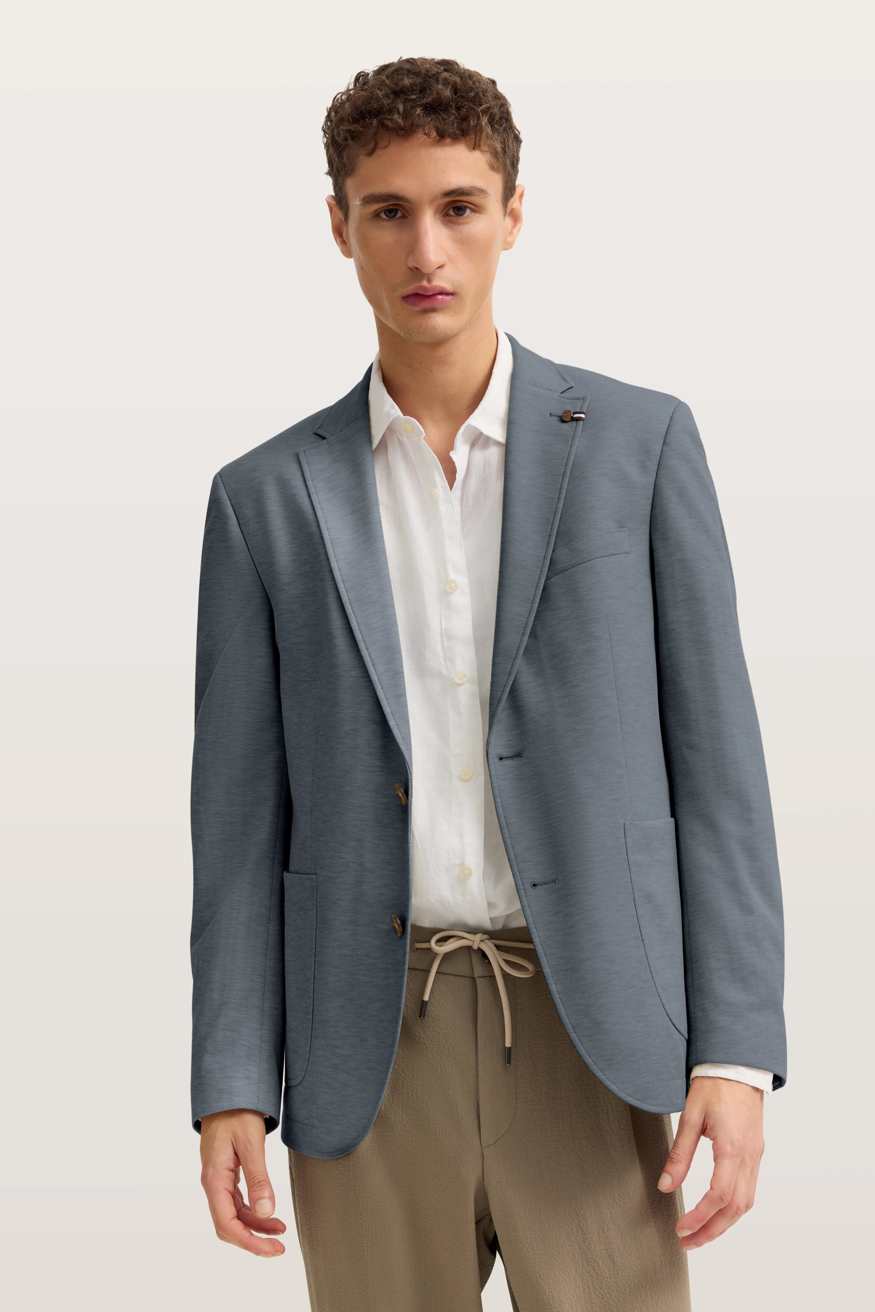 bugatti Modelbild in blauem Blazer, weißem Hemd und beigen Hosen, entspanntes Posing.
