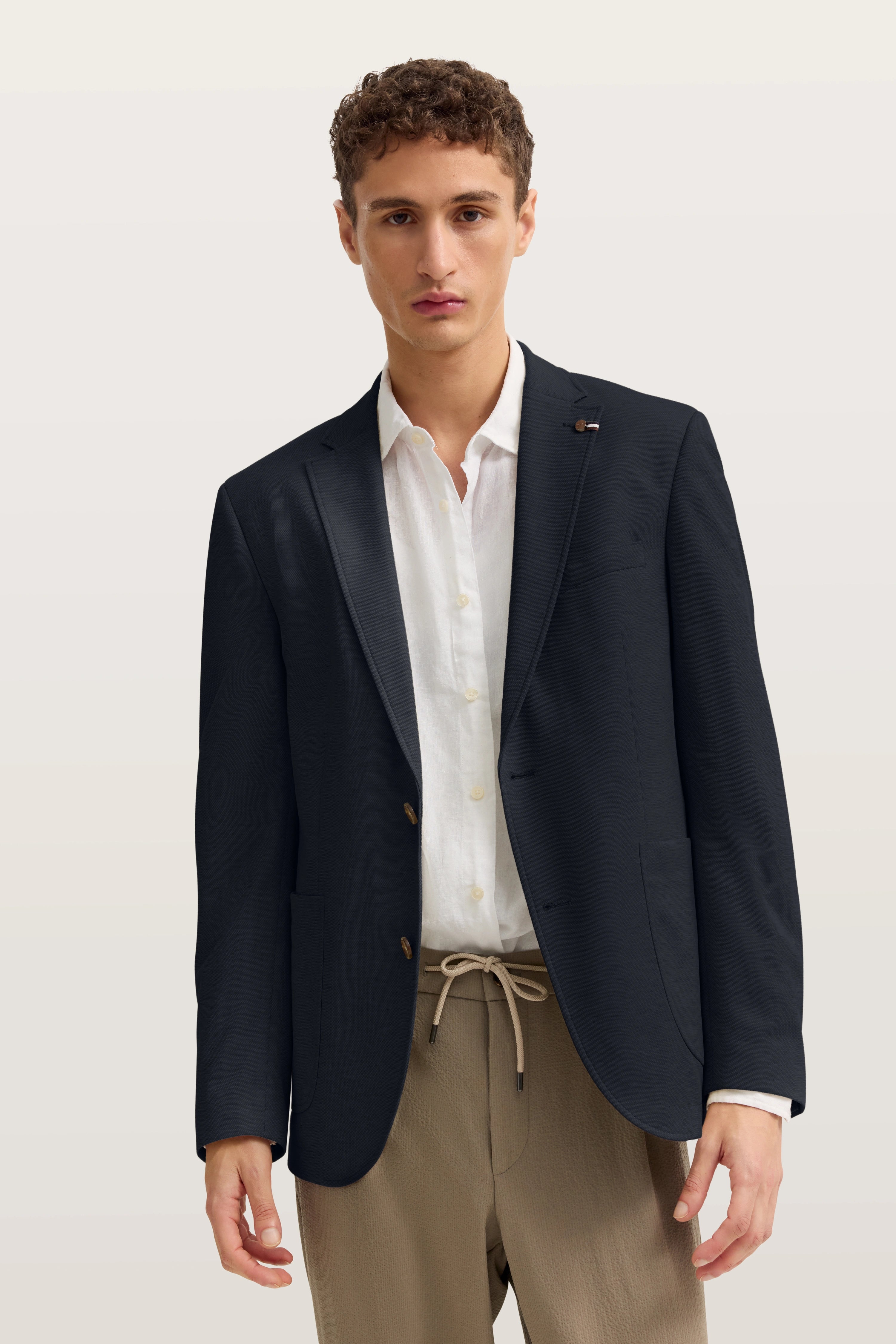Model trägt schwarzes Sakko, weißes Hemd, beige Hose von bugatti, lässige Pose.